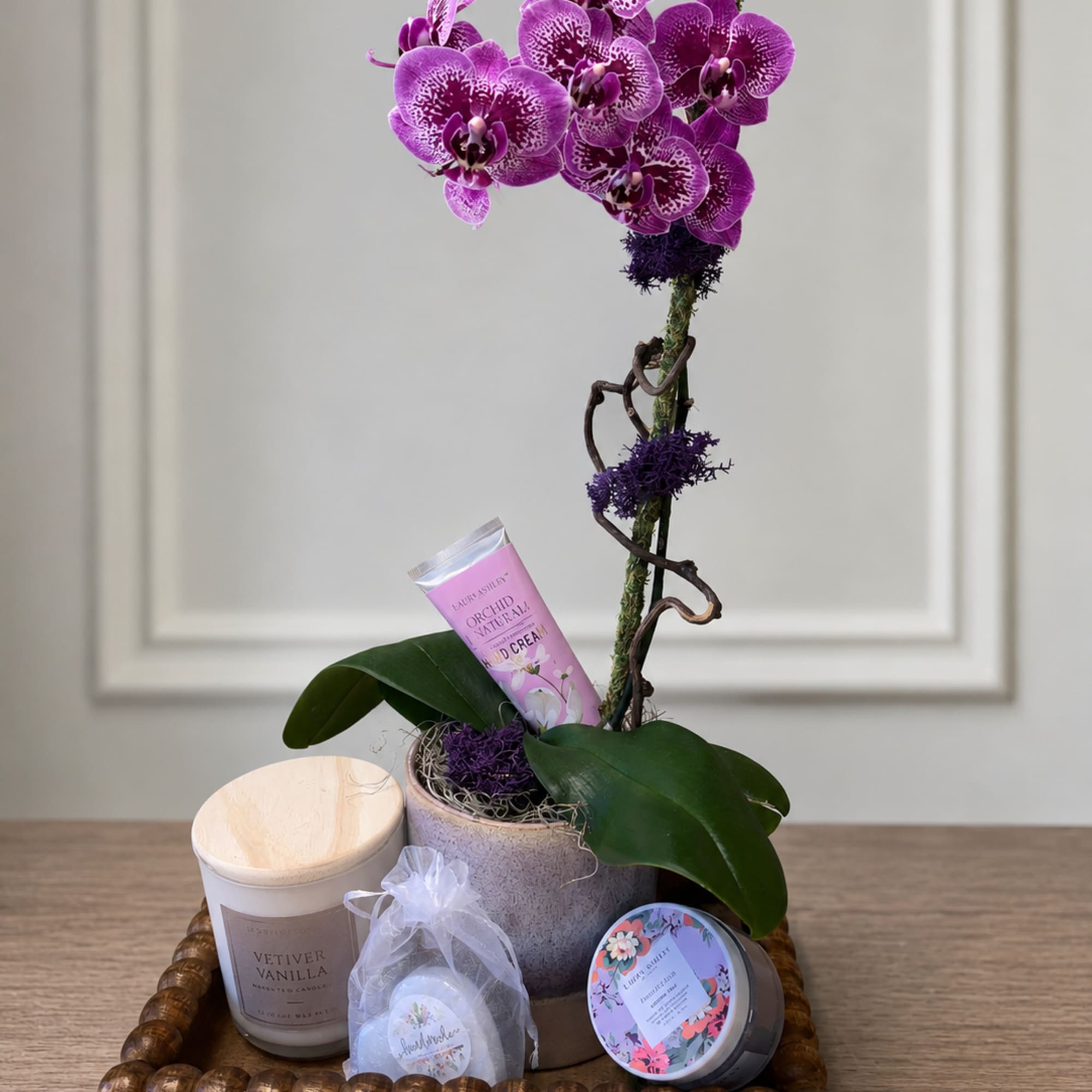 Purple orchid arrangement with candles and bath items in a wooden tray