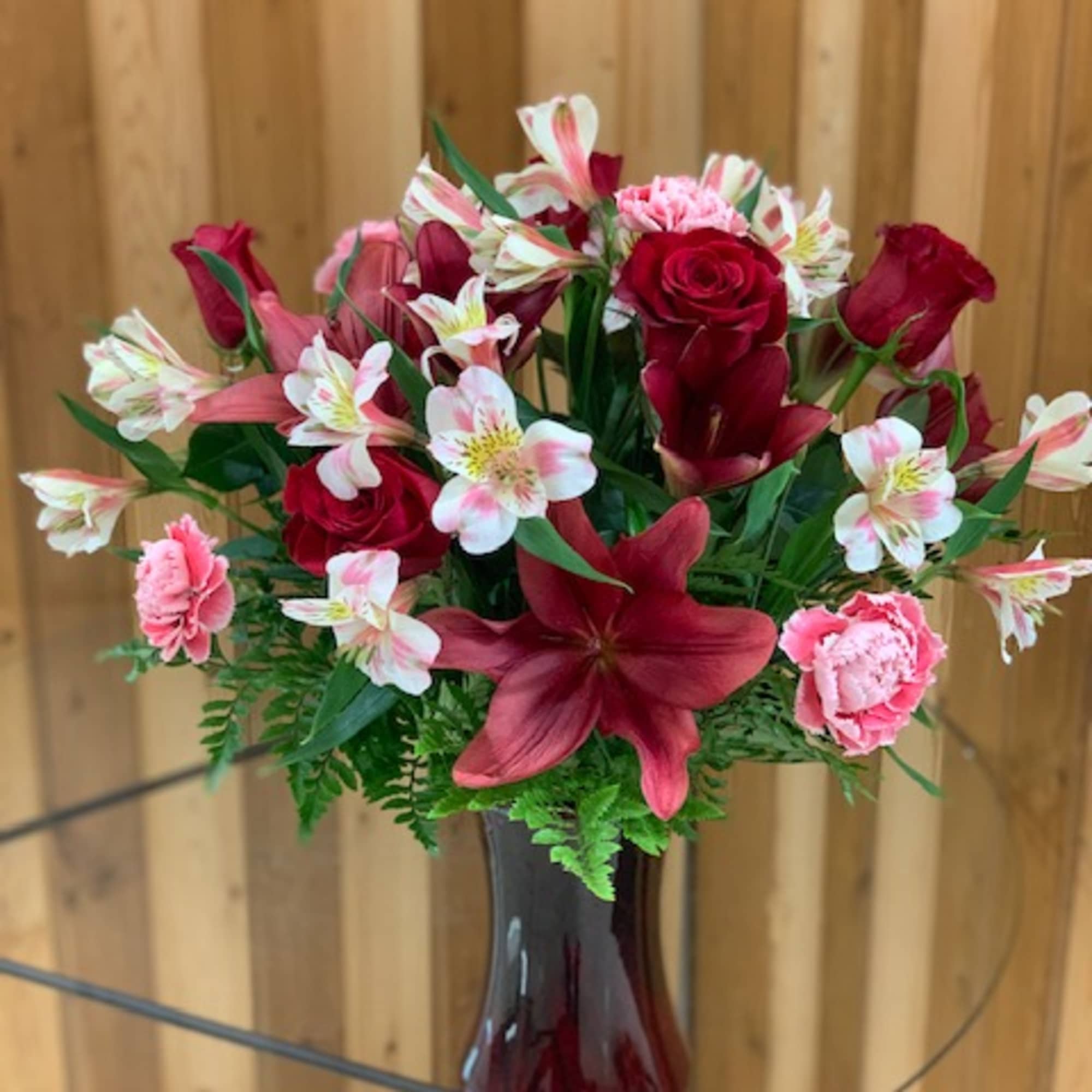 Red roses and pink lilies arranged in a dark glass vase