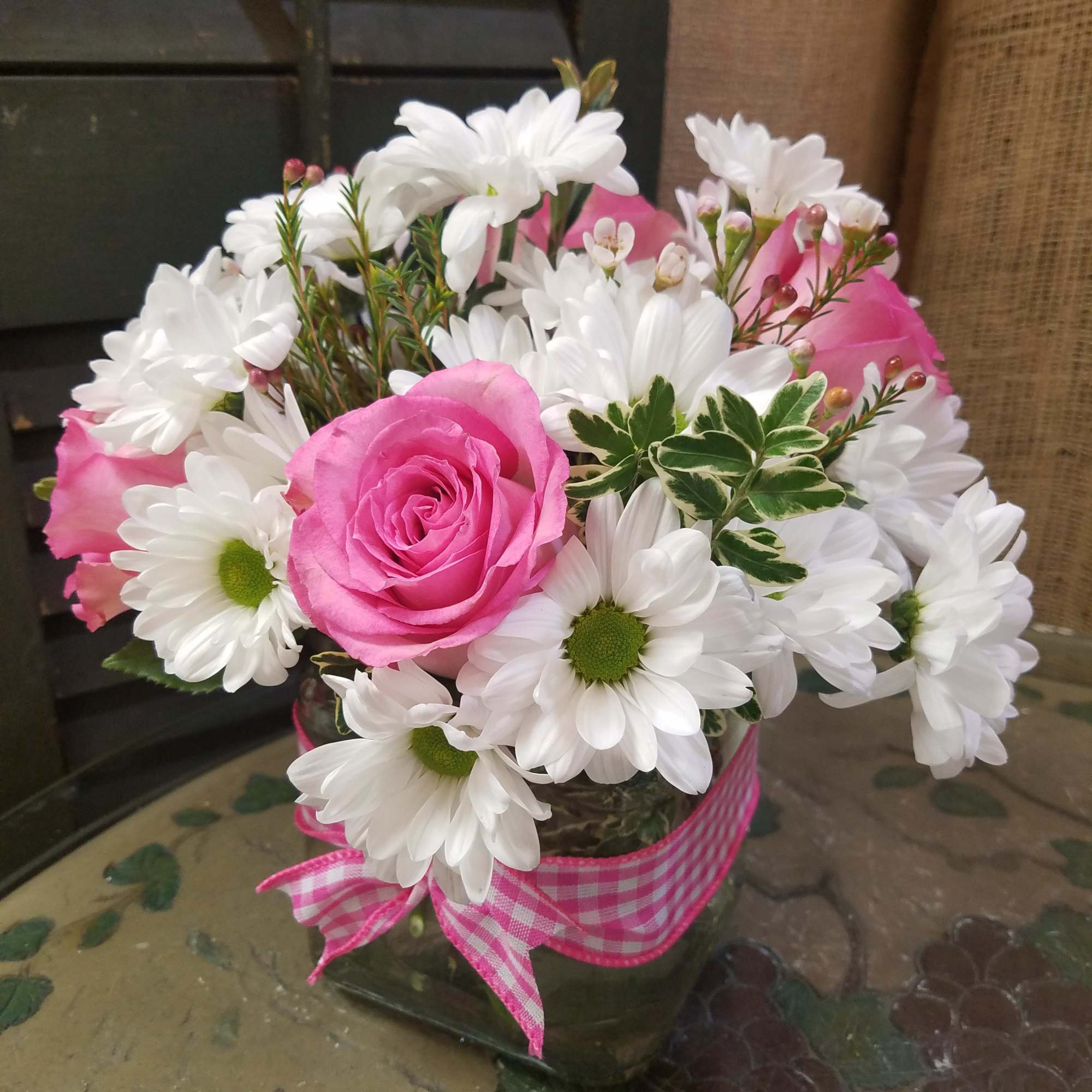 Pink roses and white daisies in a glass vase with a pink ribbon