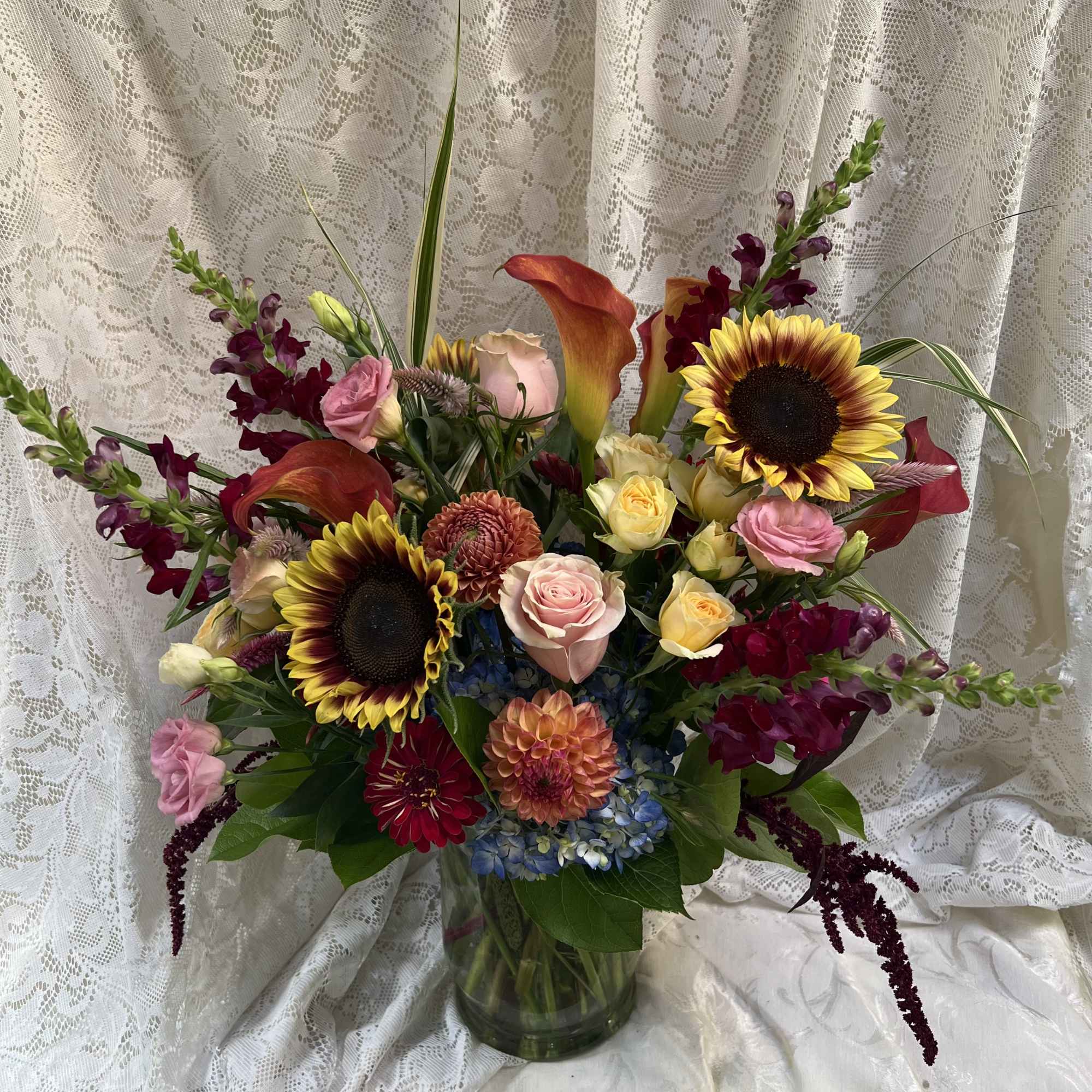 Mixed bouquet with sunflowers, roses, calla lilies, and orchids in a glass vase