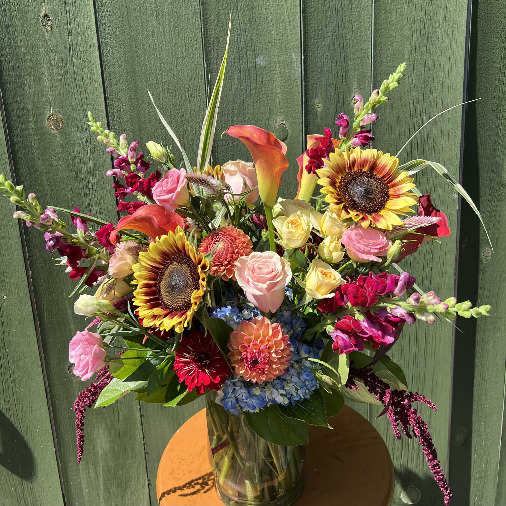 Mixed bouquet with sunflowers, roses, calla lilies, and snapdragons in a glass vase