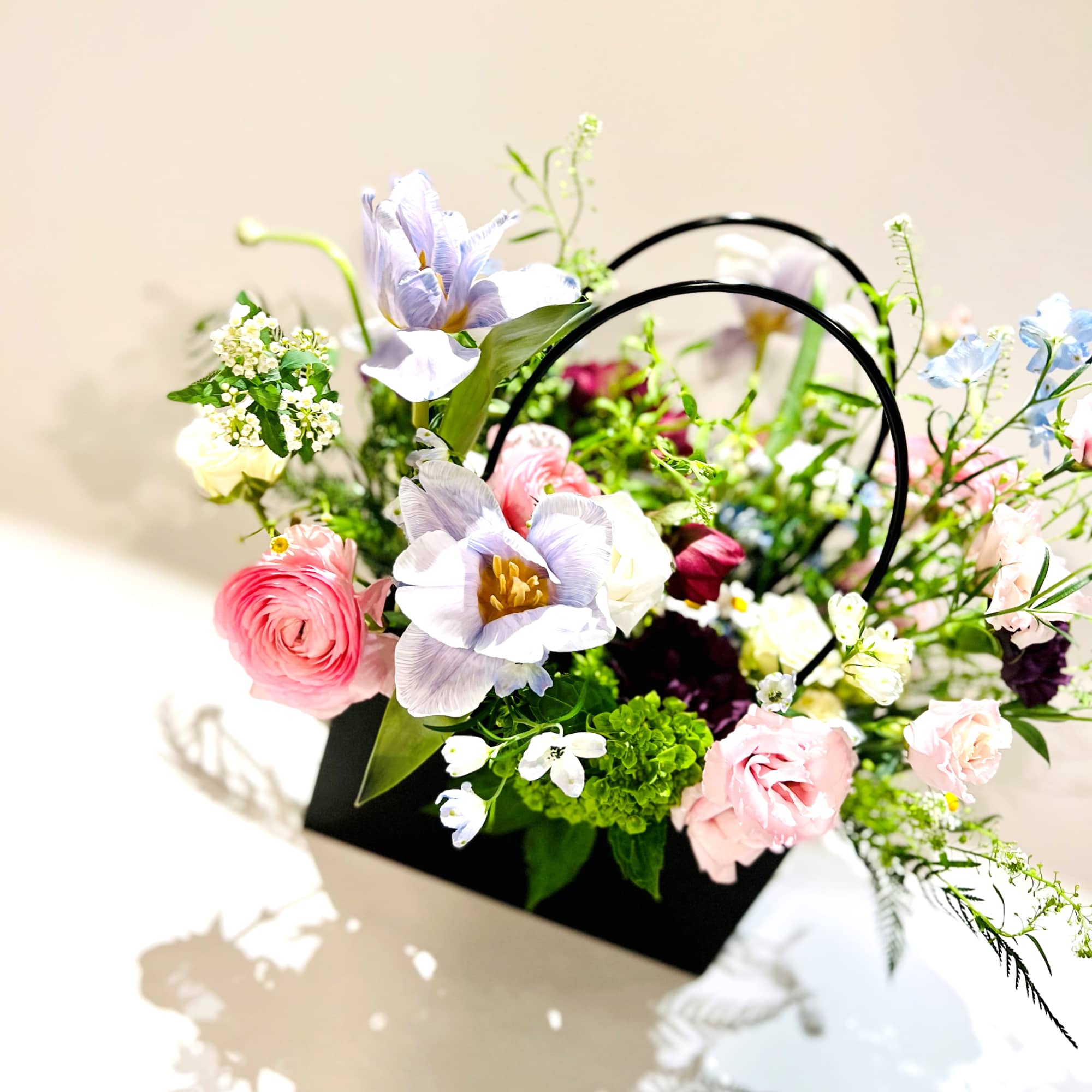 Mixed pastel flowers in a black handled basket