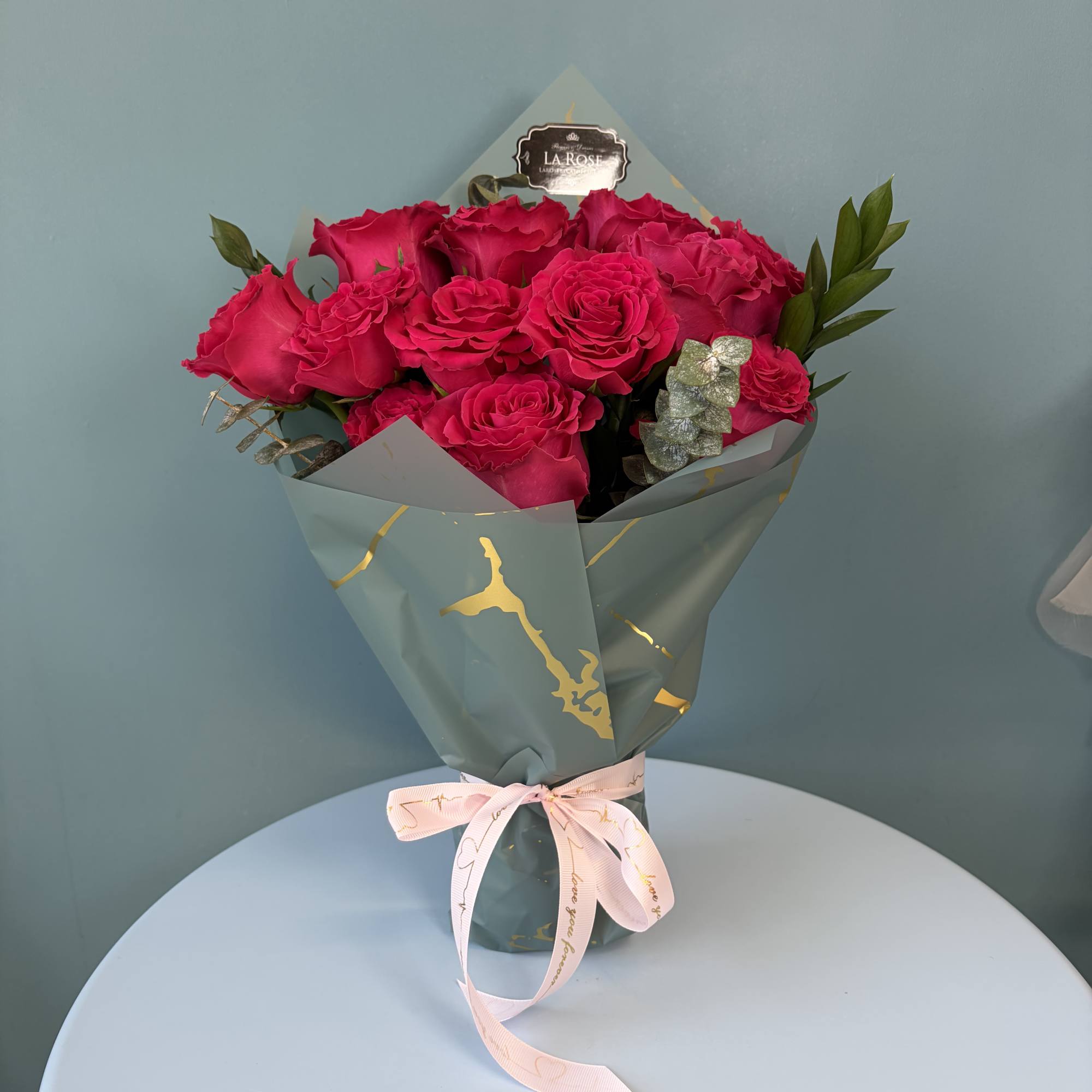 Bouquet of hot pink roses wrapped in blue paper with a pink ribbon
