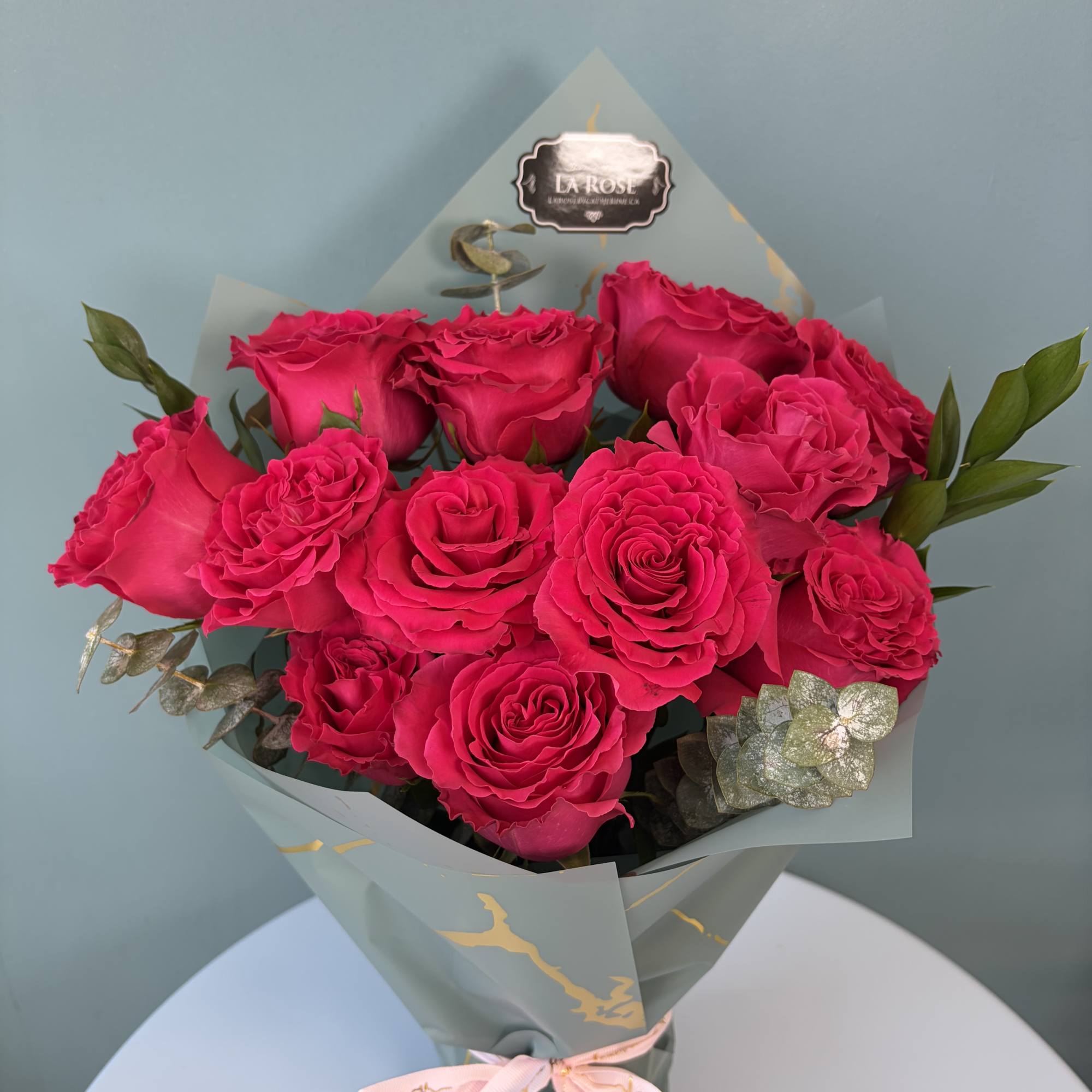 Bouquet of hot pink roses wrapped in pale blue paper with a pink ribbon
