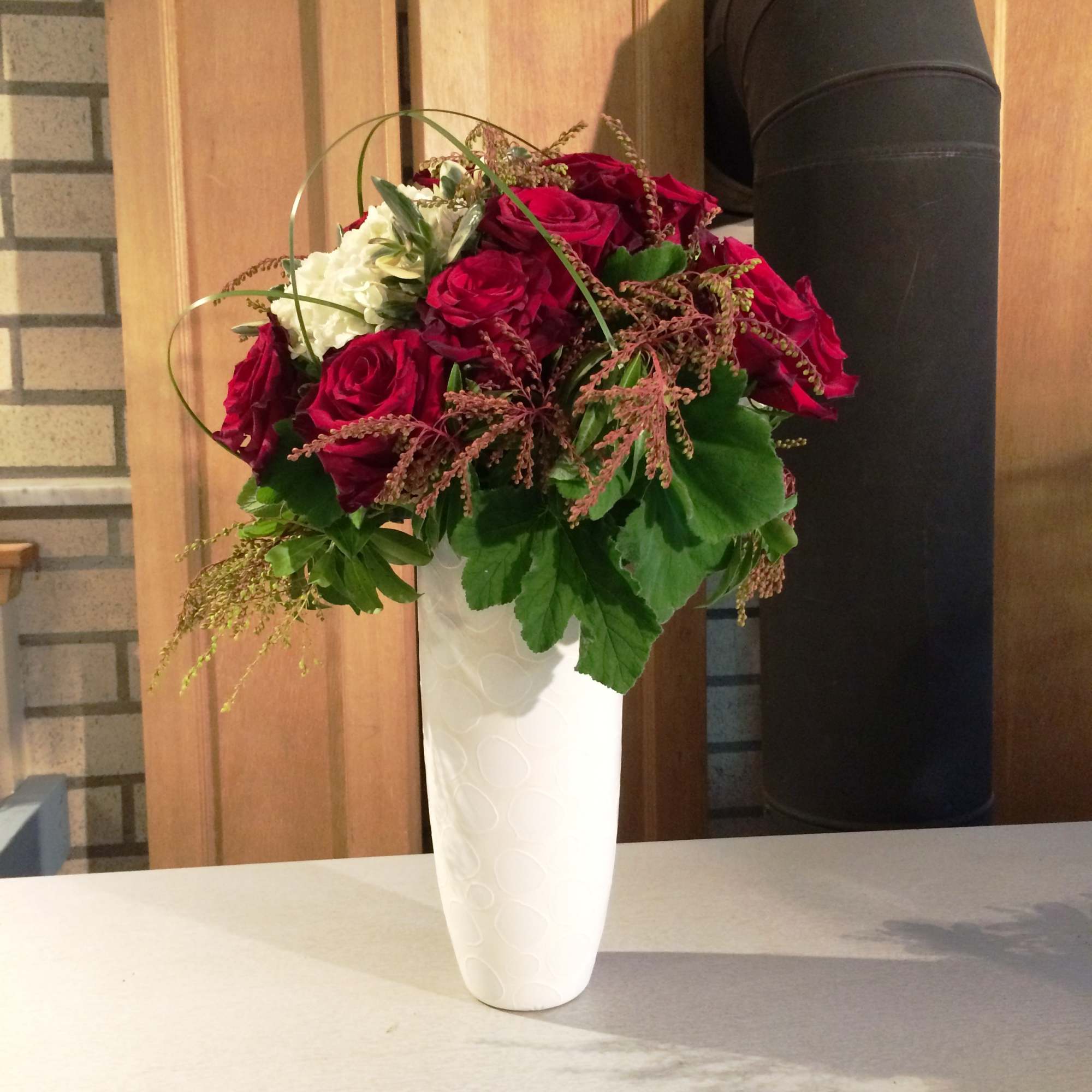 Red roses and white flowers in a tall white vase