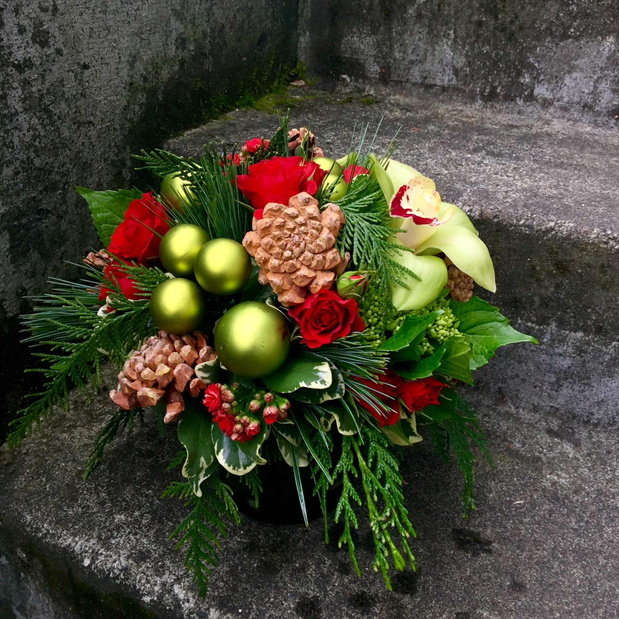 Red roses and pinecones arranged with green ornaments in a low bouquet