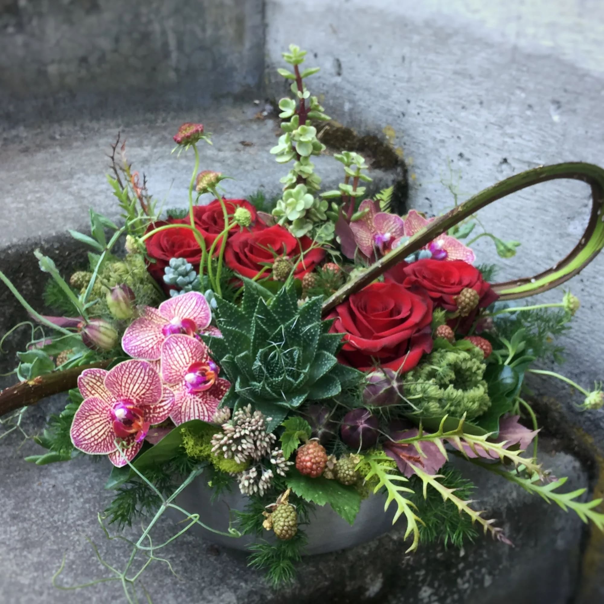 Mixed floral arrangement with red roses and pink orchids in a low container