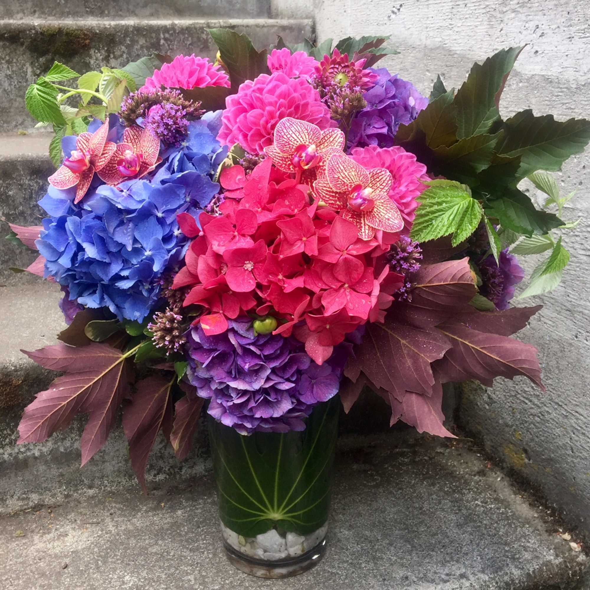 Bright hydrangea bouquet in a glass vase with orchids and dark foliage