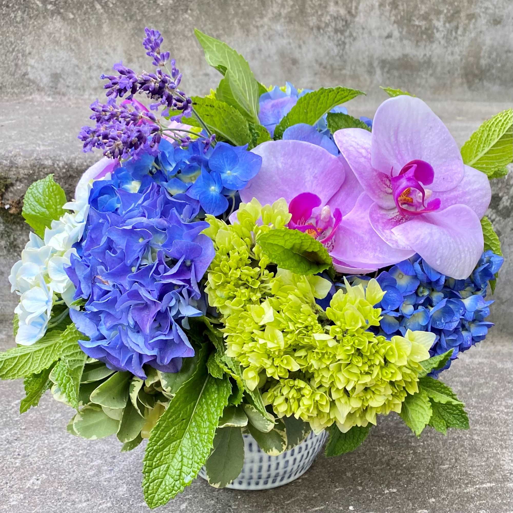 Blue and purple hydrangeas with pink orchids in a patterned bowl