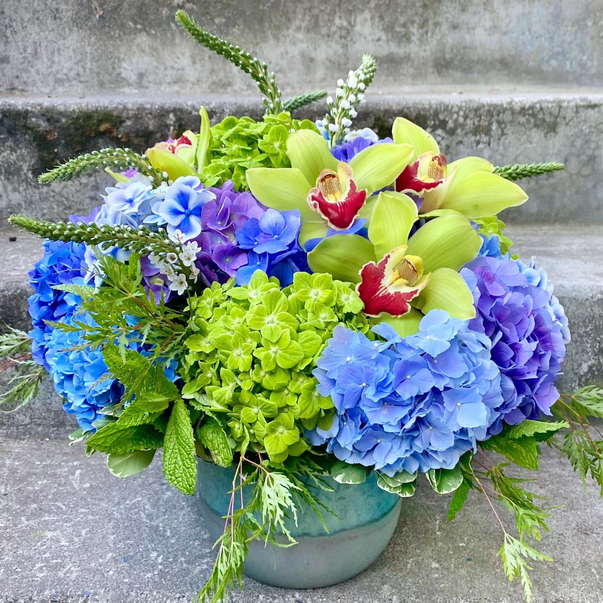 Blue and purple hydrangeas with green orchids in a ceramic pot