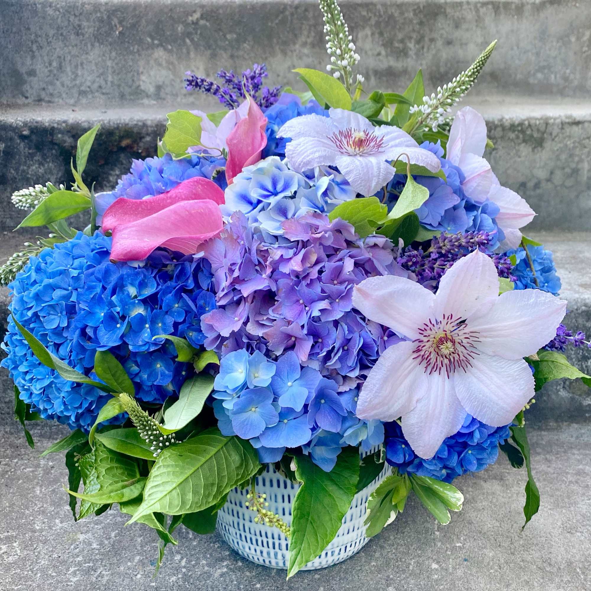 Blue and lavender flower arrangement with pink calla lilies in a patterned vase