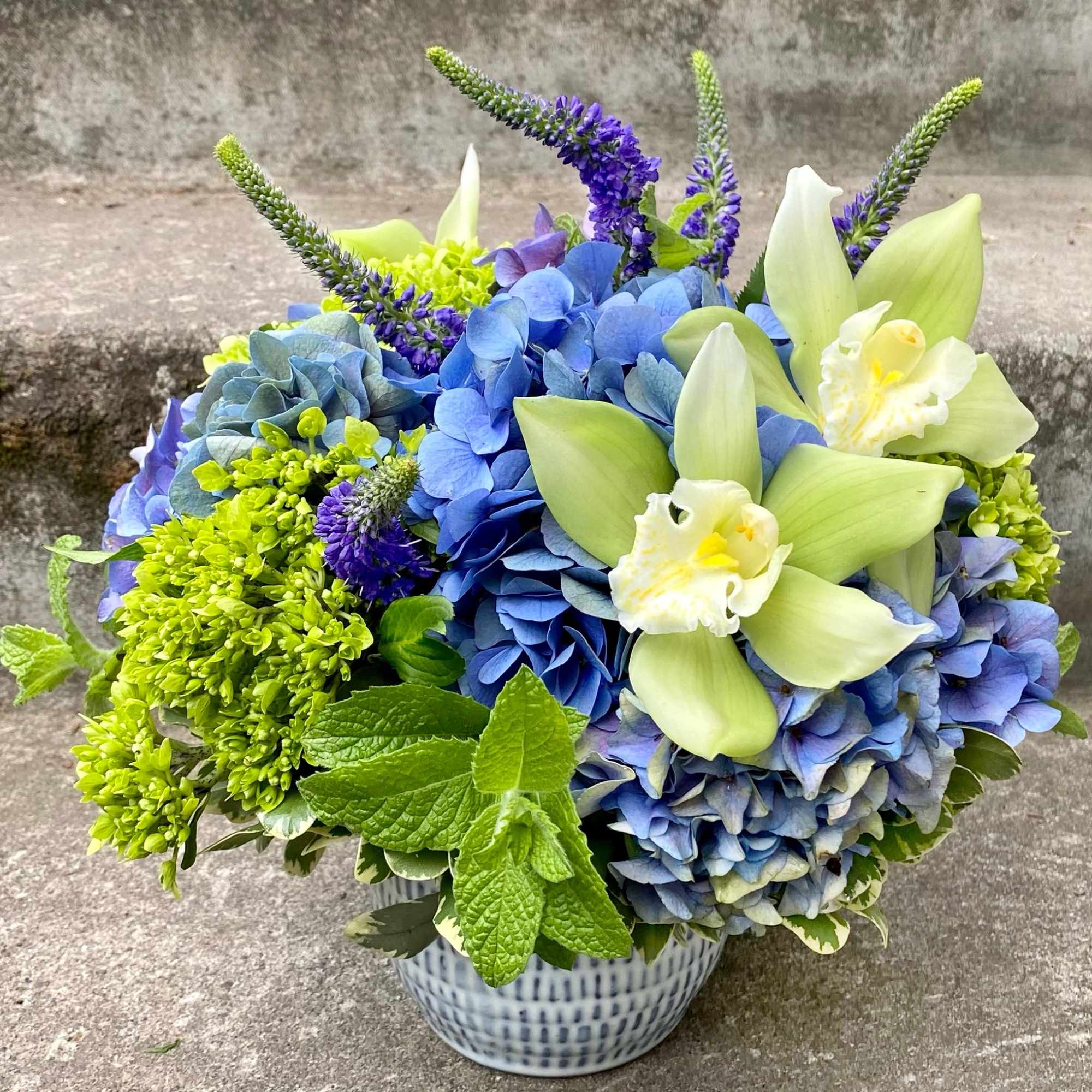 Blue hydrangeas and pale green orchids in a patterned vase