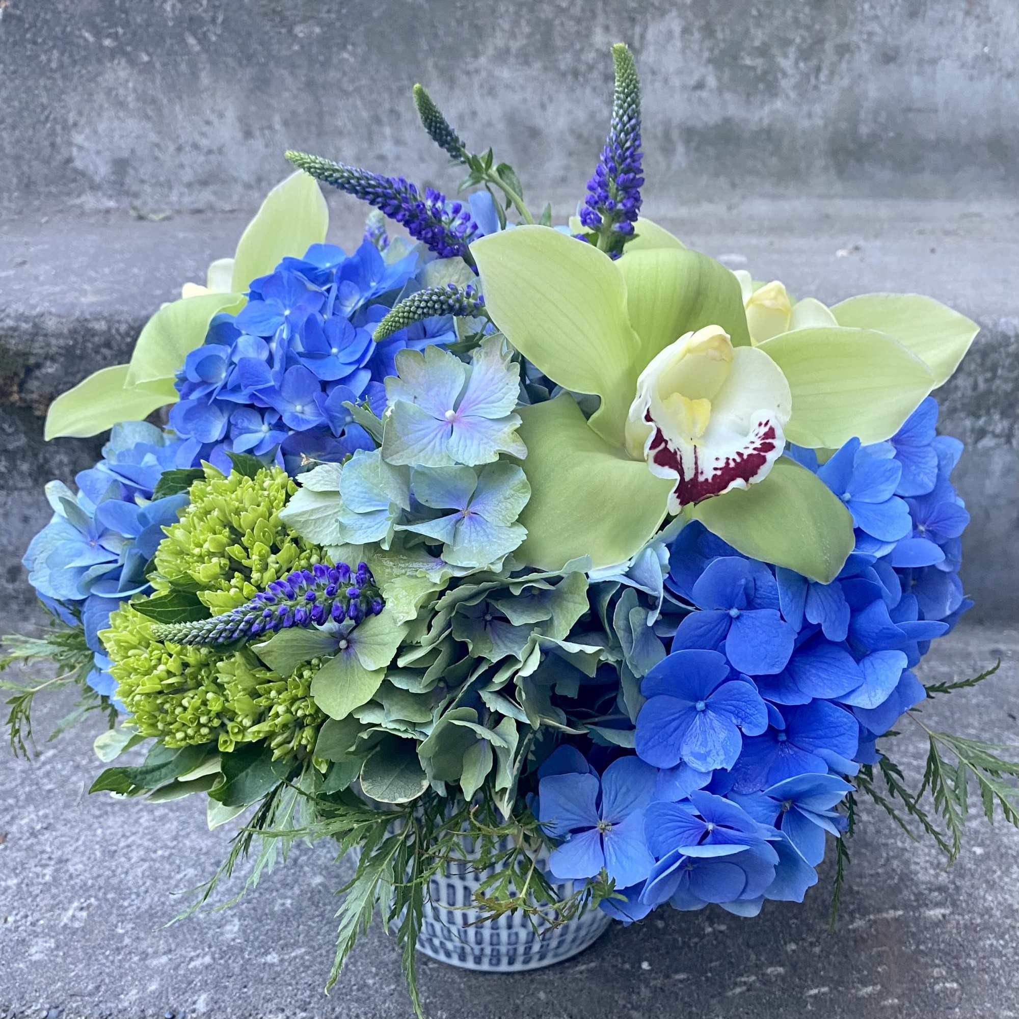 Blue hydrangeas and green orchids in a patterned vase