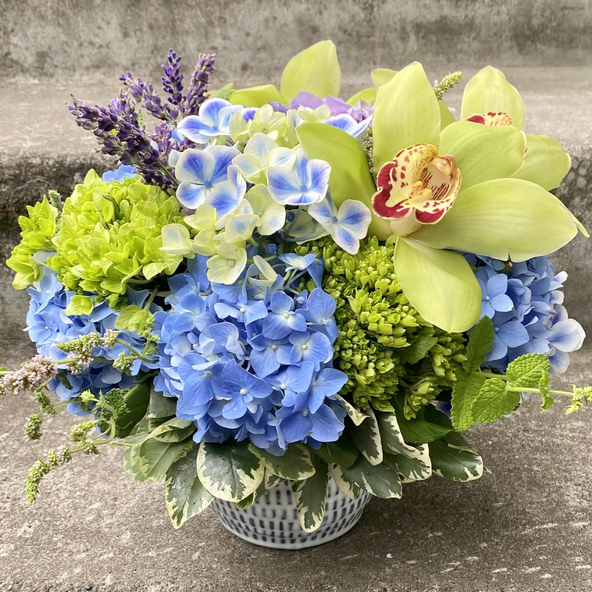 Blue and green floral arrangement in a patterned ceramic bowl