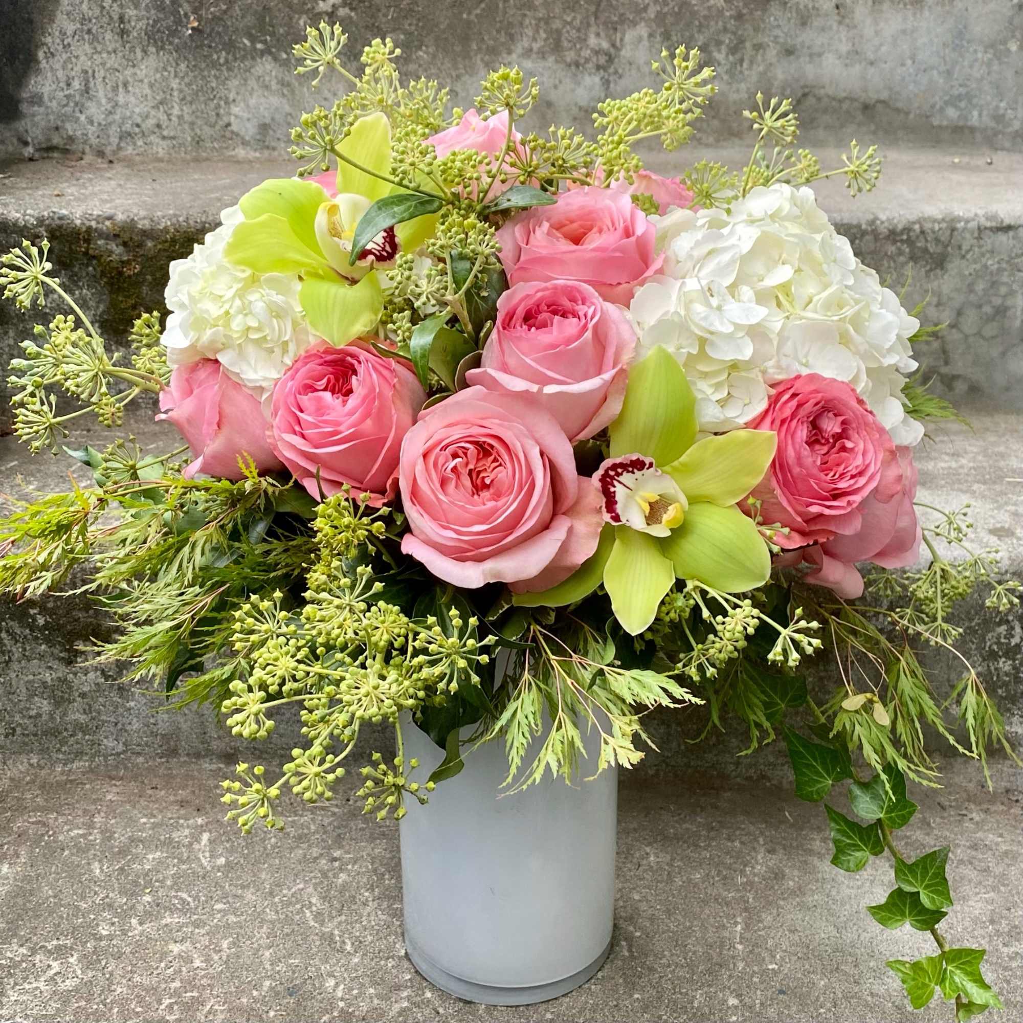 Pink roses and white hydrangeas in a white vase with green orchids