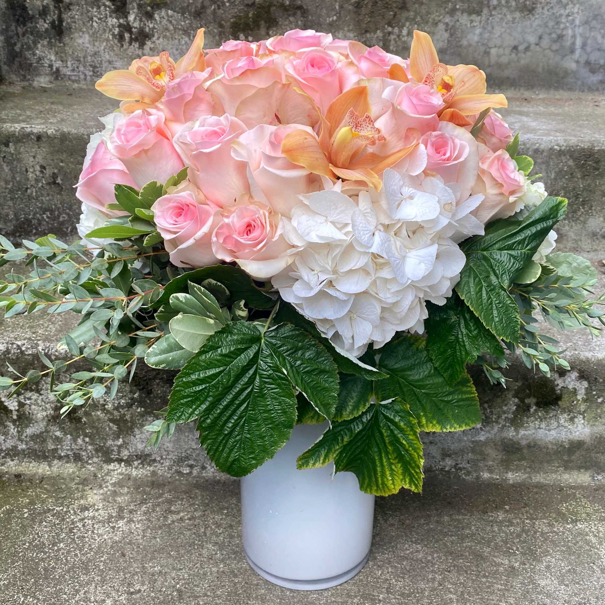 Pink roses and white hydrangeas in a white vase with orange orchids