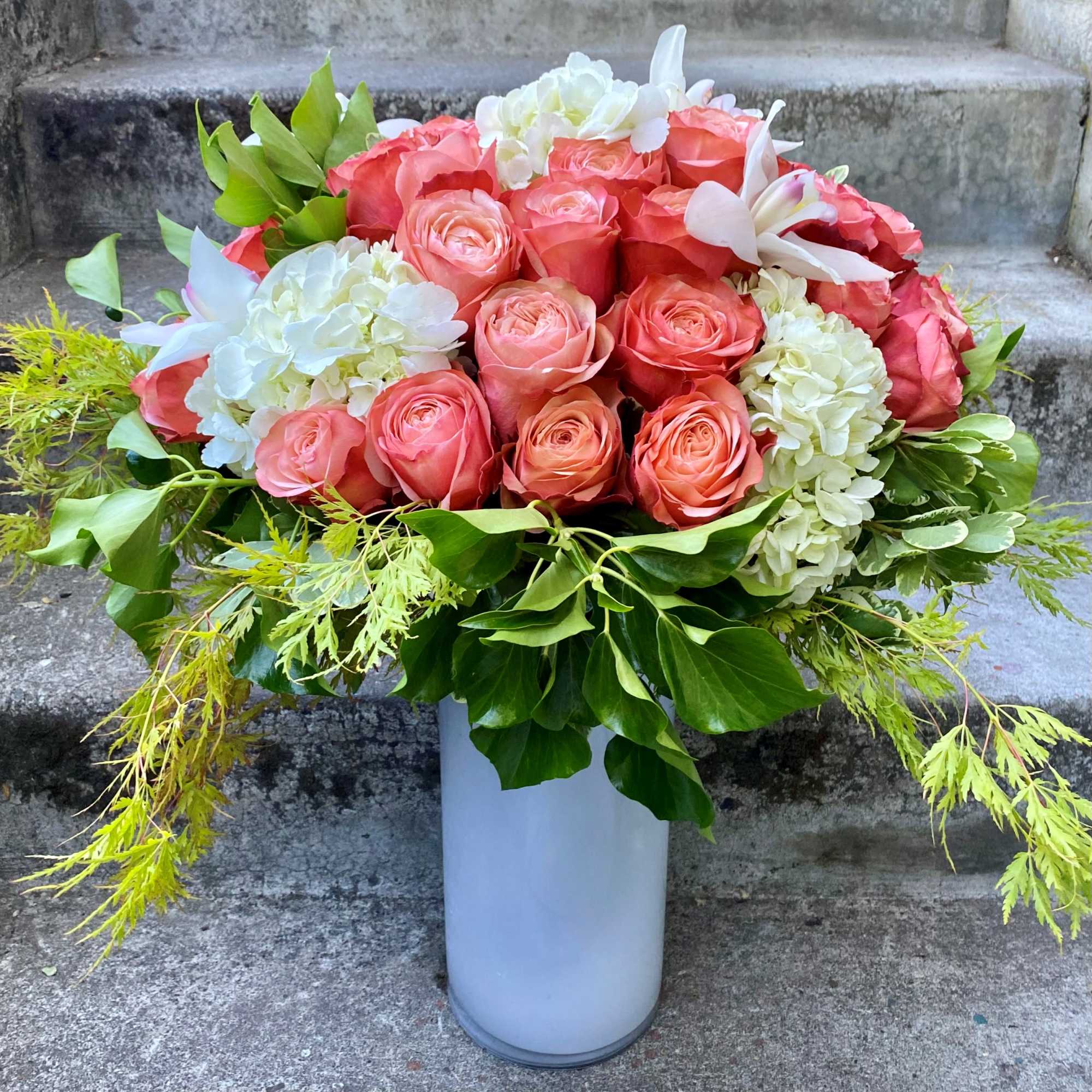 Coral roses and white hydrangeas in a tall white vase