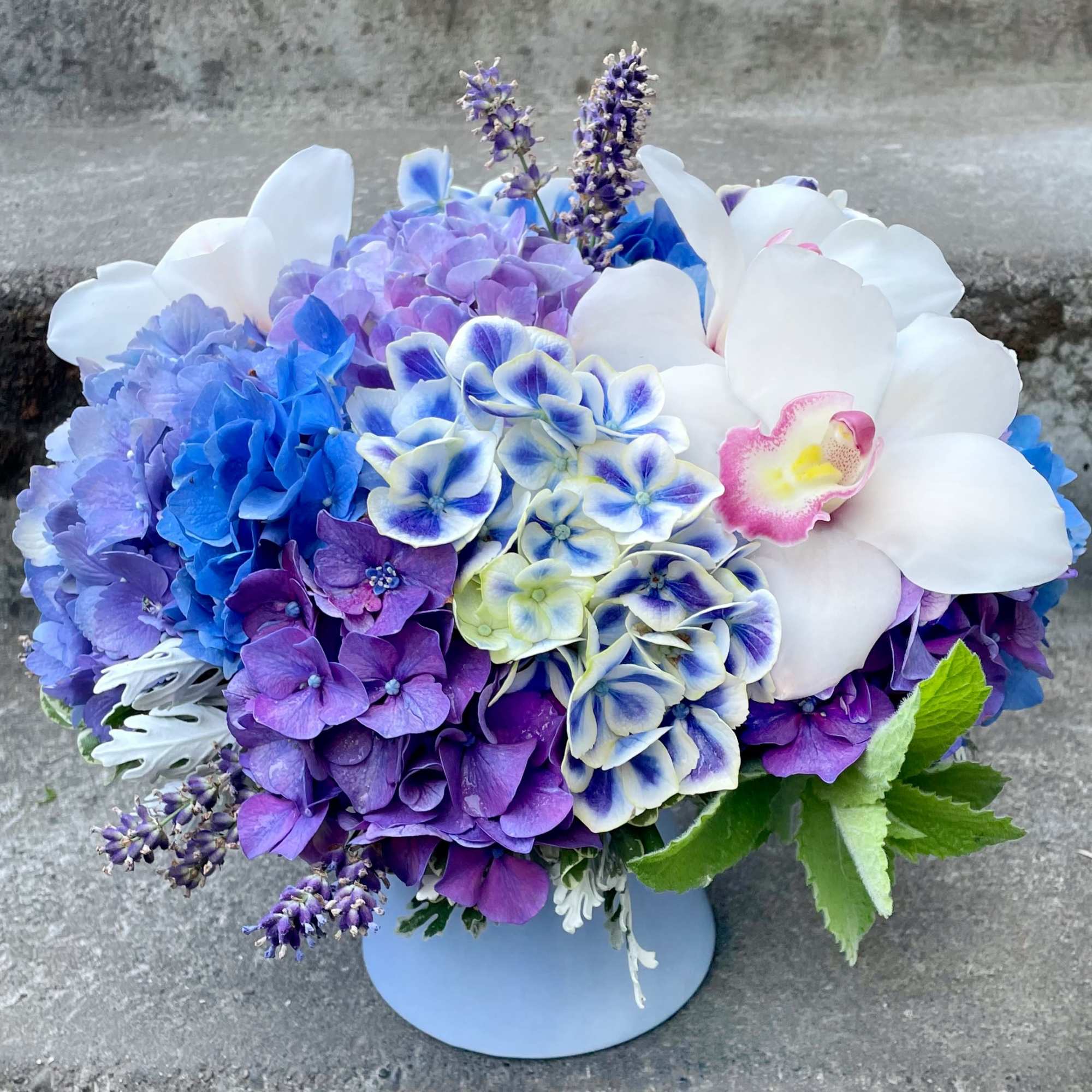 Blue, purple, and white floral arrangement in a round vase