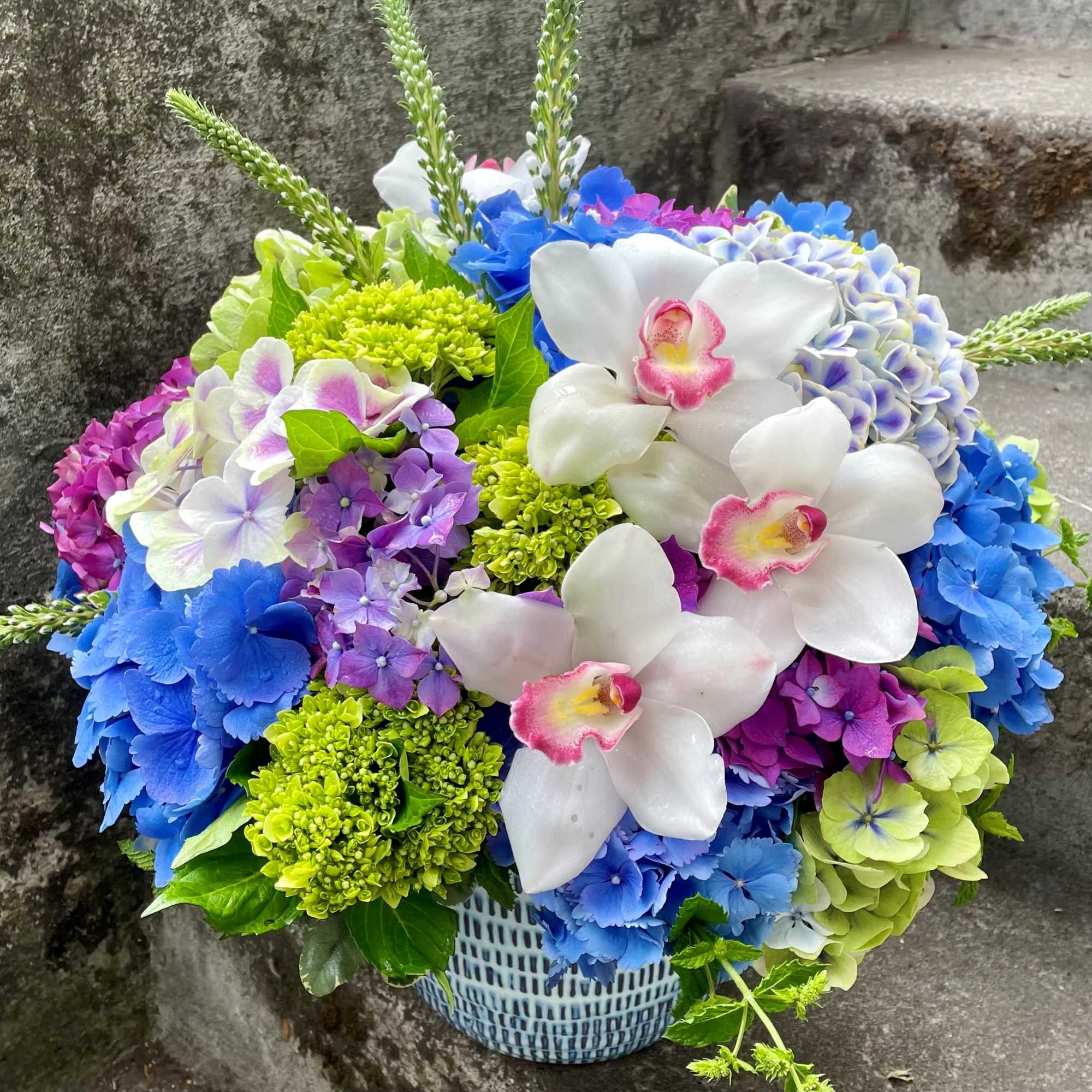 Colorful bouquet with white orchids and blue, purple, and green blooms in a basket