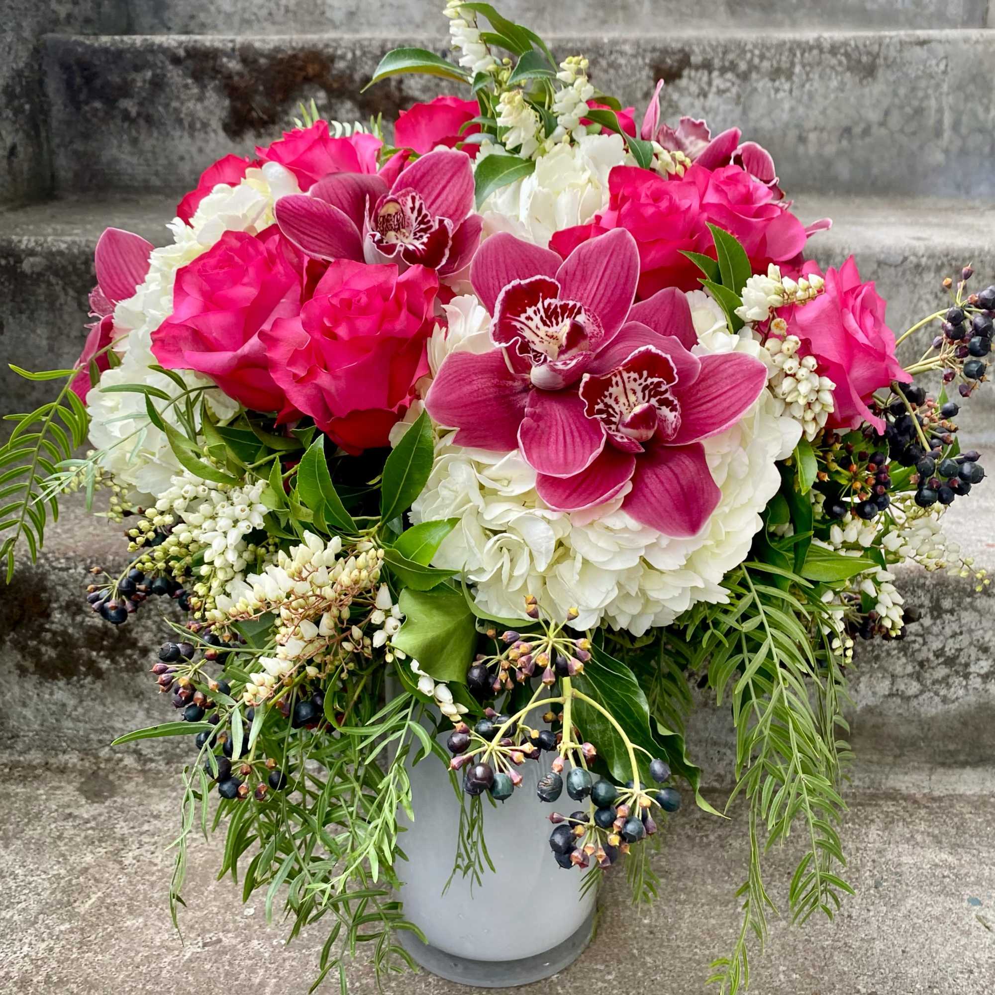 Pink orchids and roses arranged in a white vase