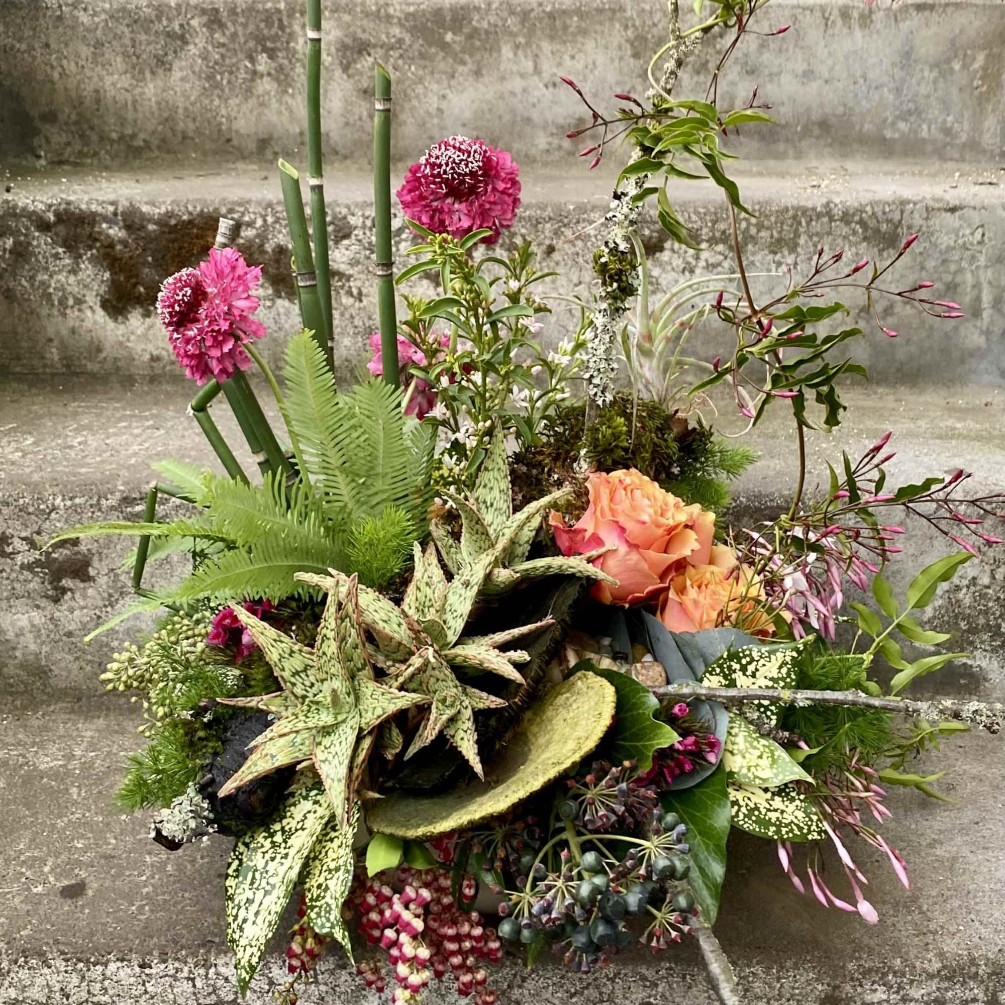 Mixed floral arrangement with pink blooms and peach roses in a low design
