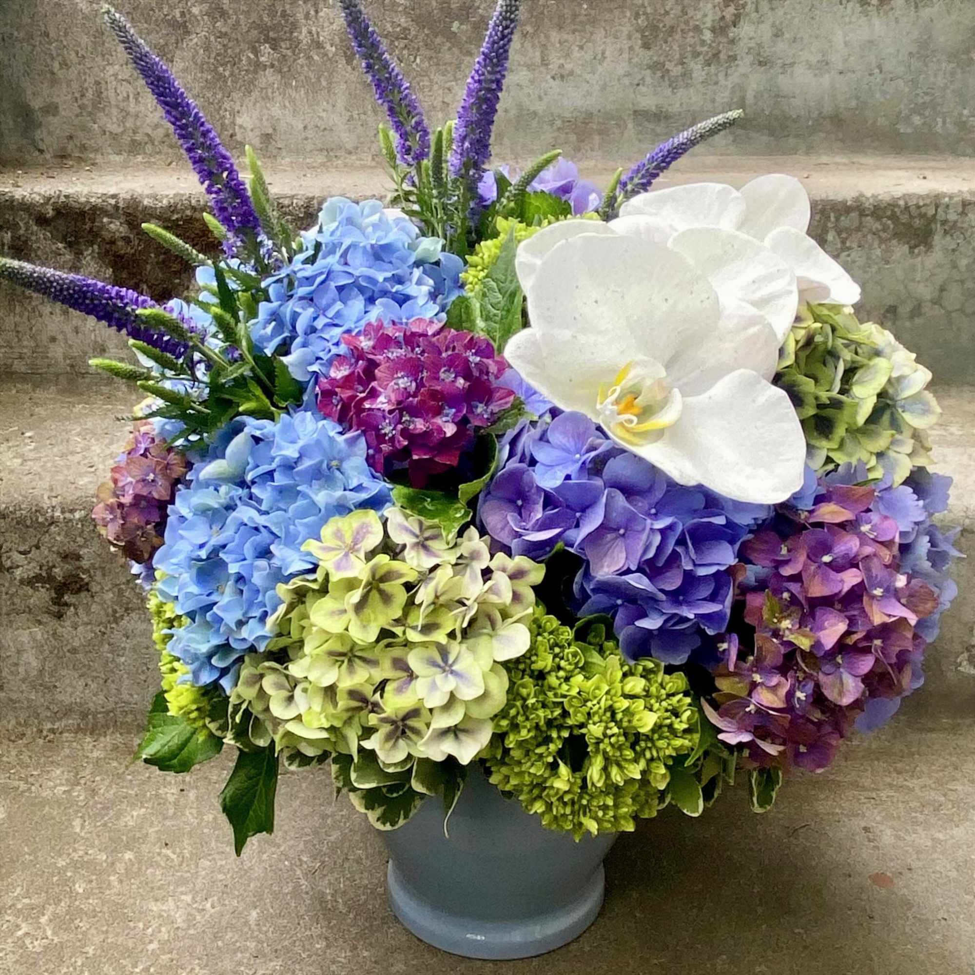 Colorful hydrangea arrangement with a white orchid in a gray vase