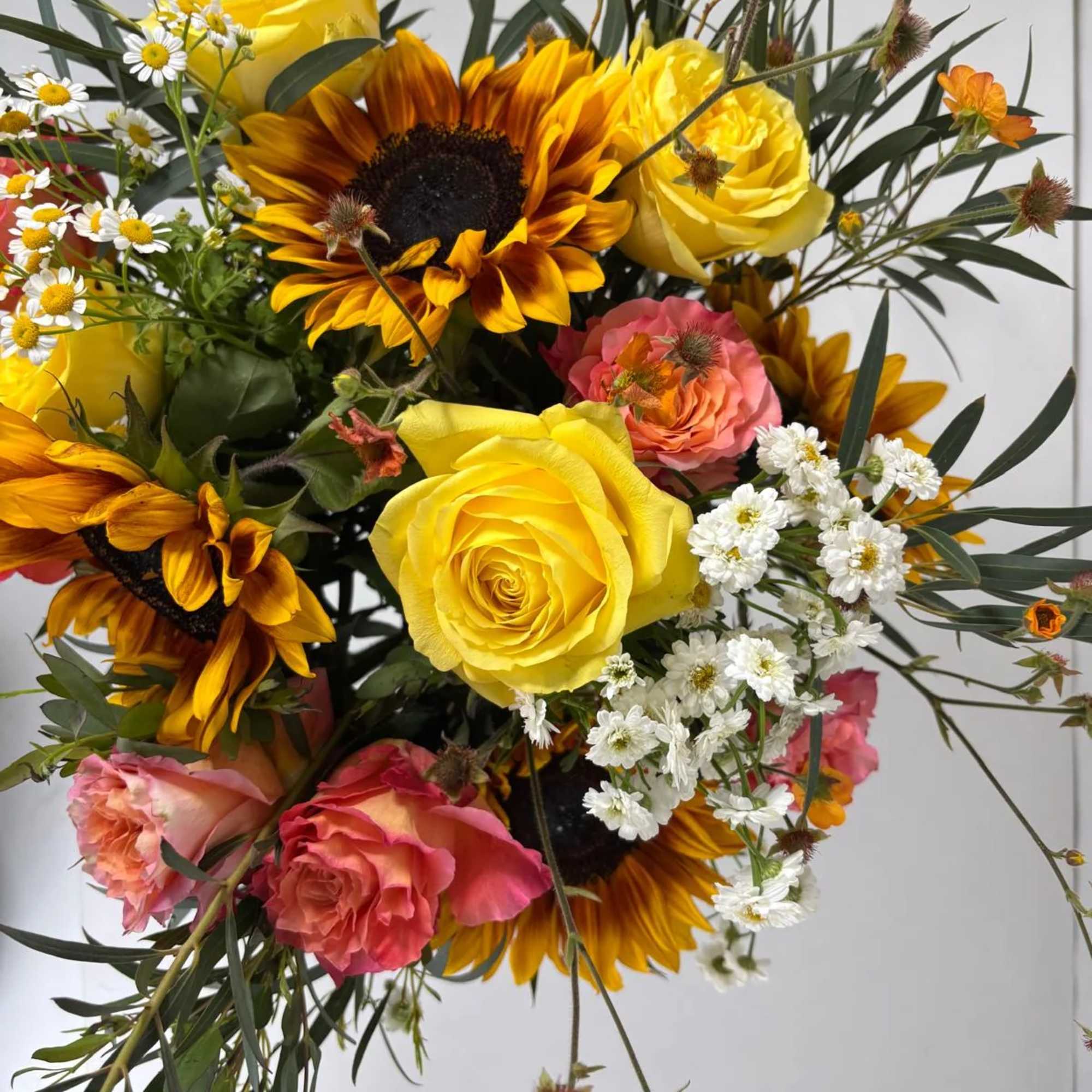 Bouquet of yellow roses, sunflowers, and pink roses with small white daisies