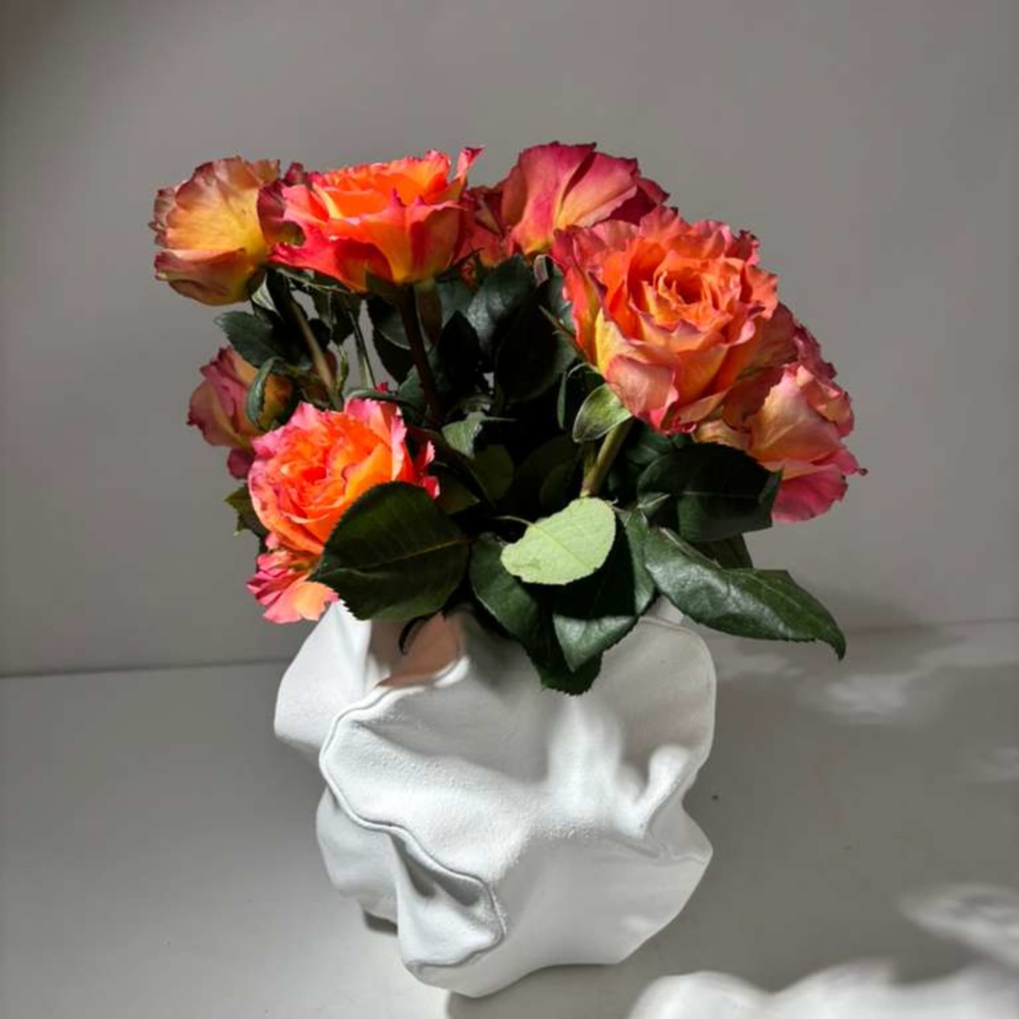 Bouquet of orange and pink roses in a white sculptural vase