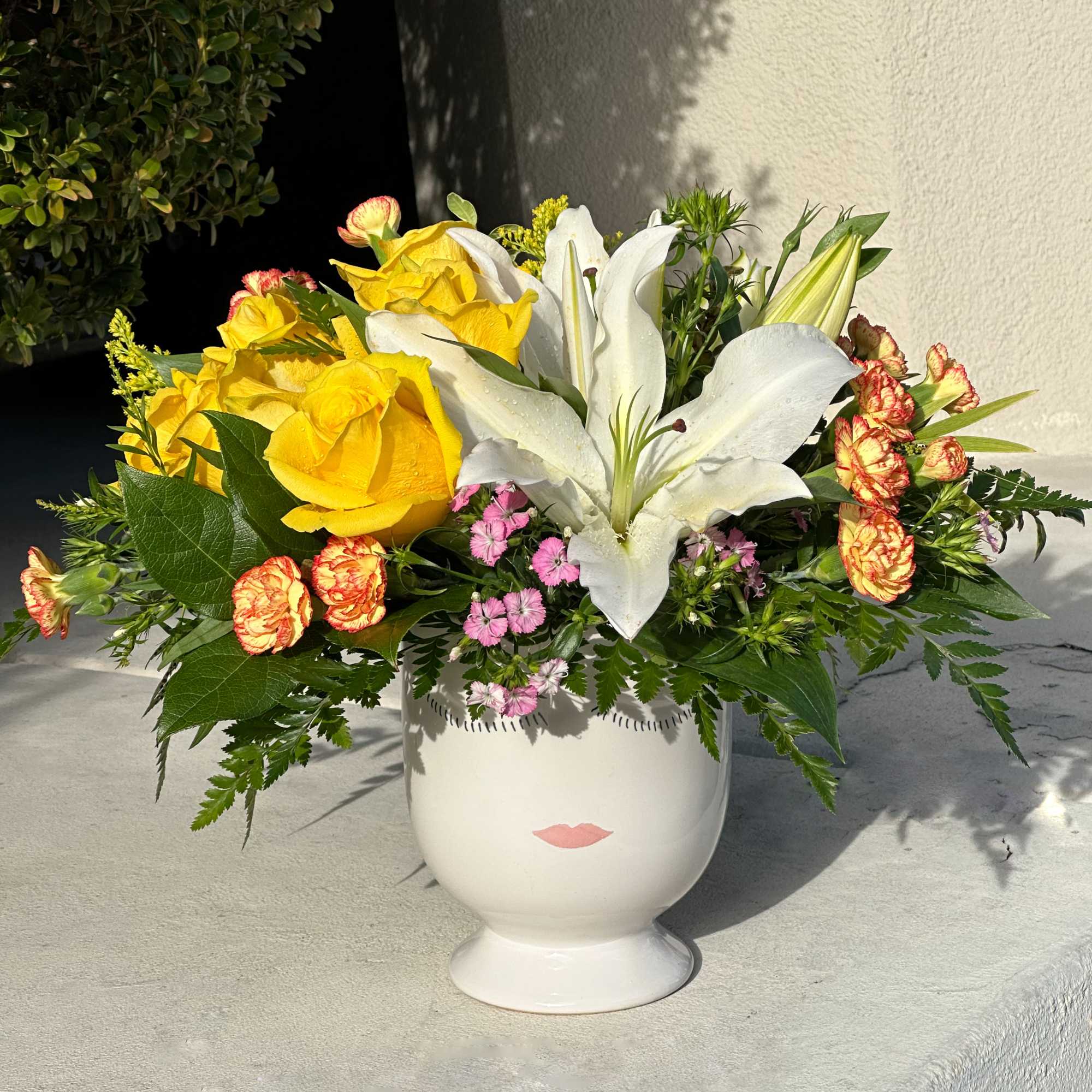 Yellow roses and white lilies in a white pedestal vase