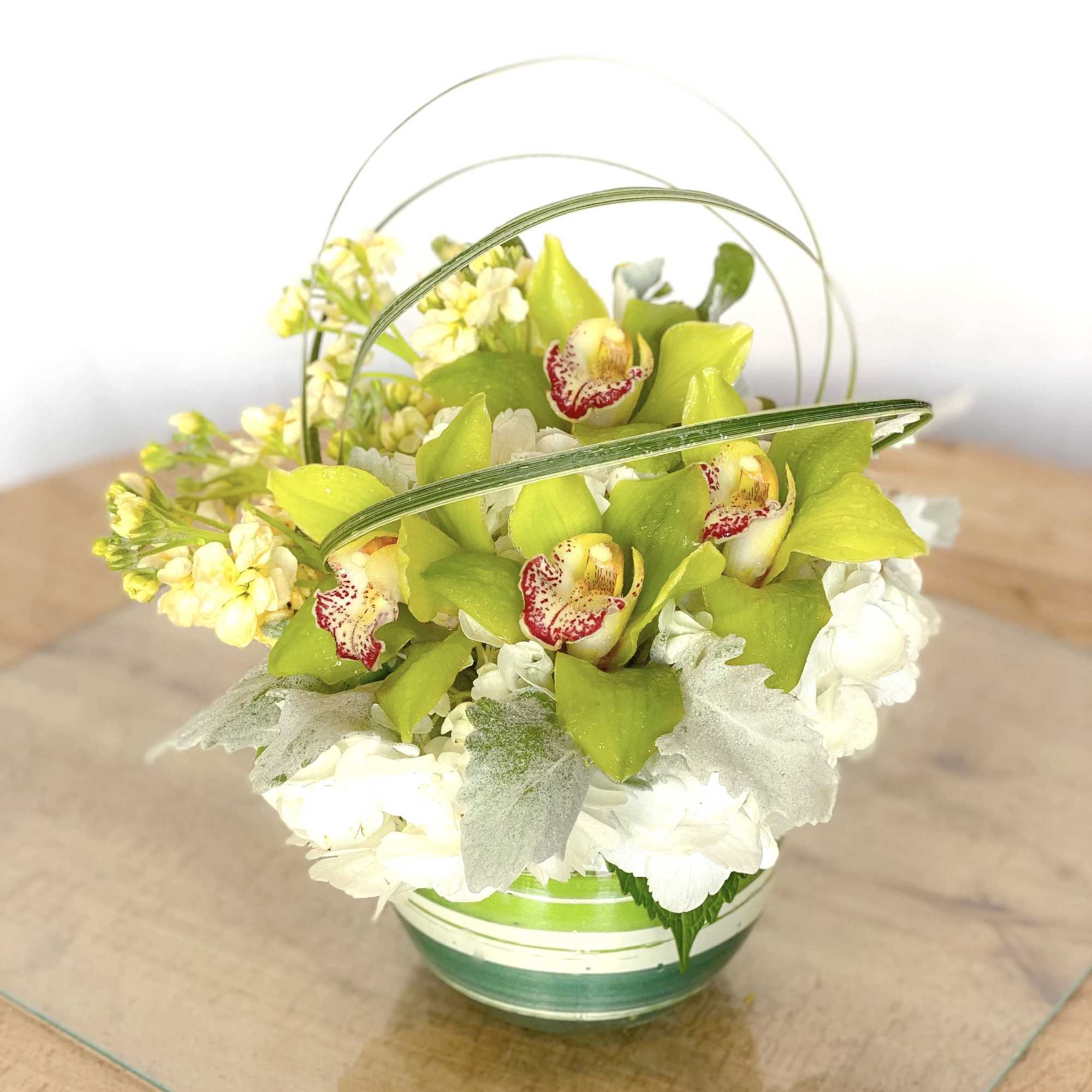 Green orchids and white flowers arranged in a glass basket vase