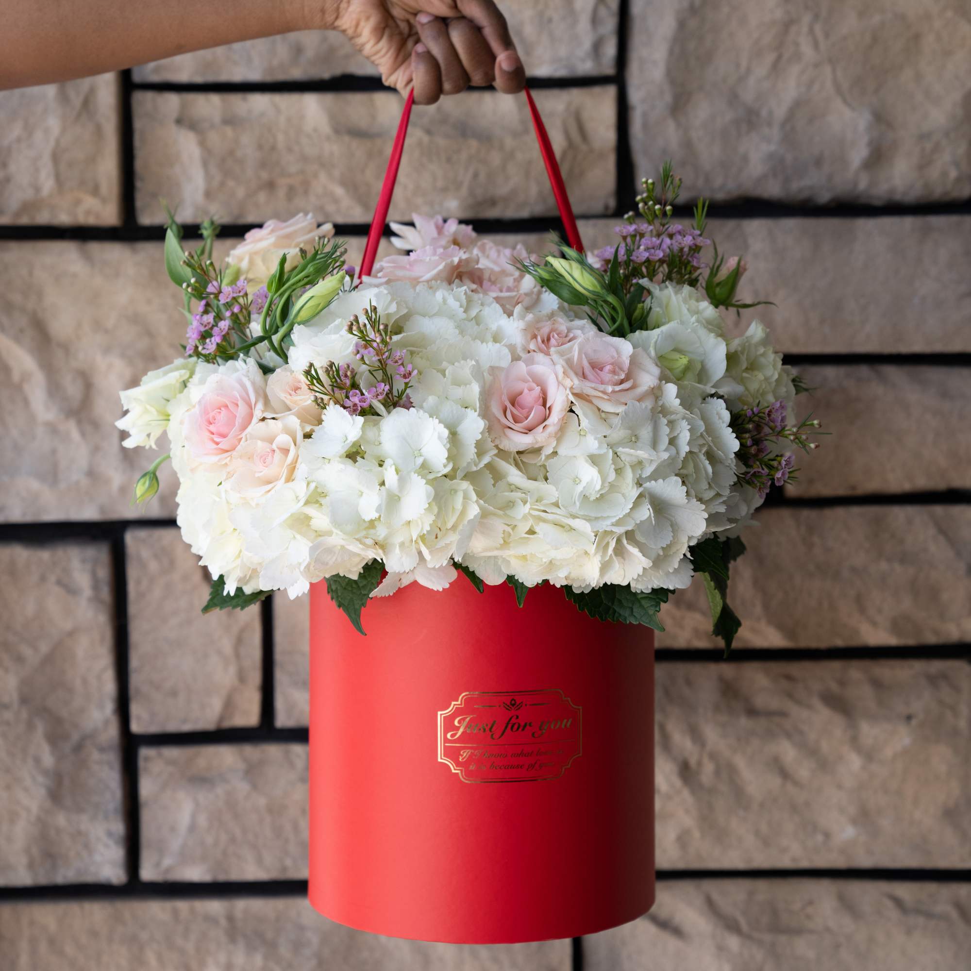 White and blush flowers arranged in a red cylindrical gift box with handles