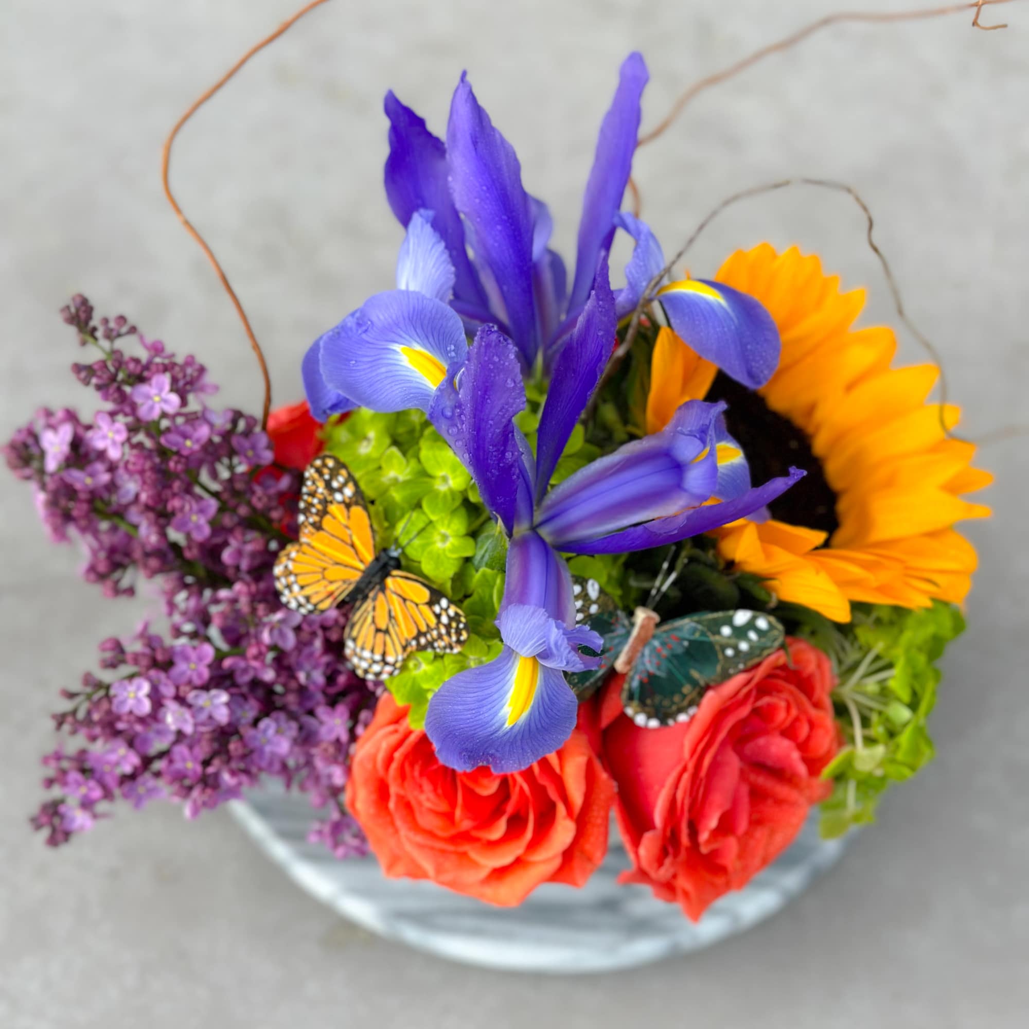 Colorful bouquet with iris, roses, sunflower, and lilac in a glass vase