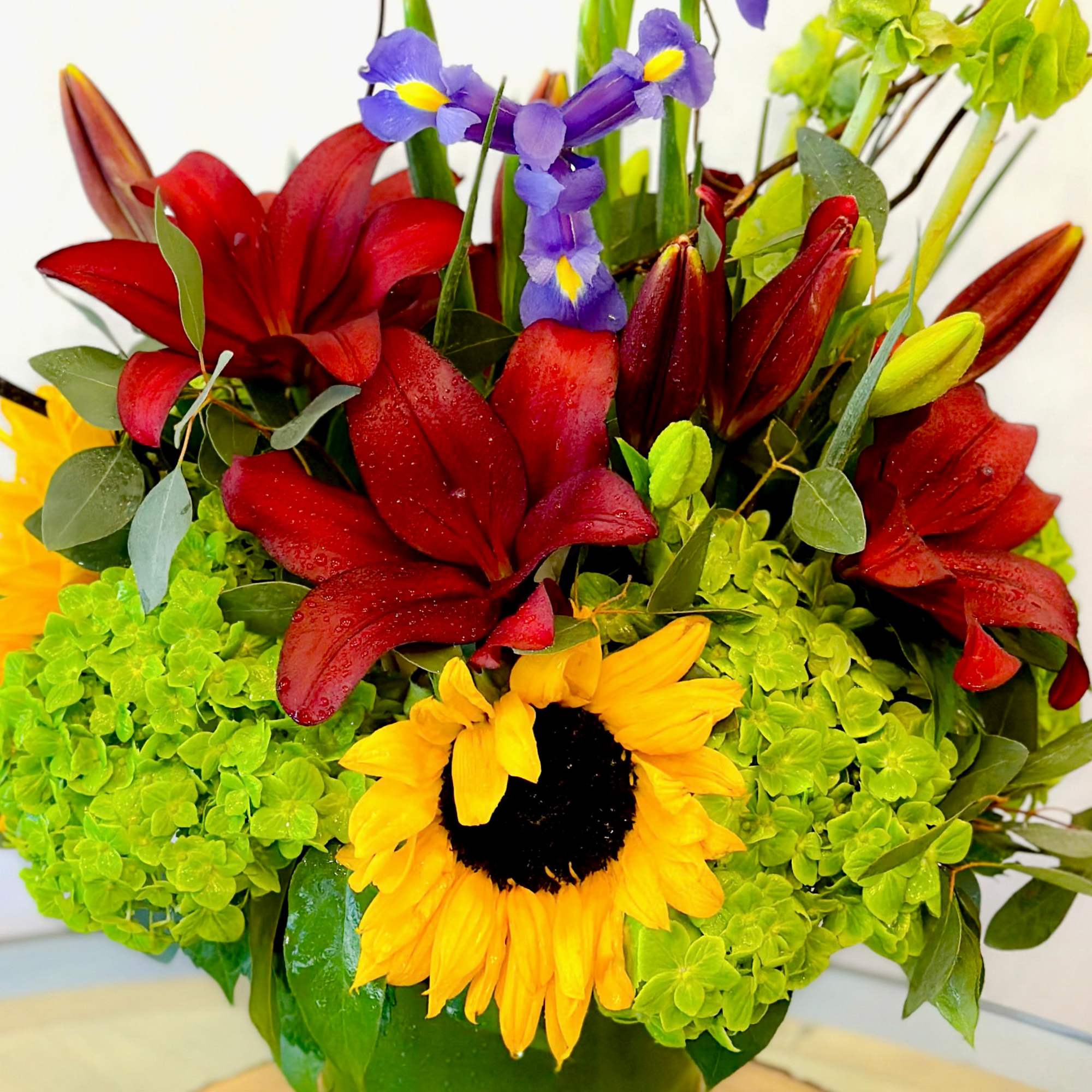 Bouquet of red lilies, yellow sunflower, and purple iris in a vase