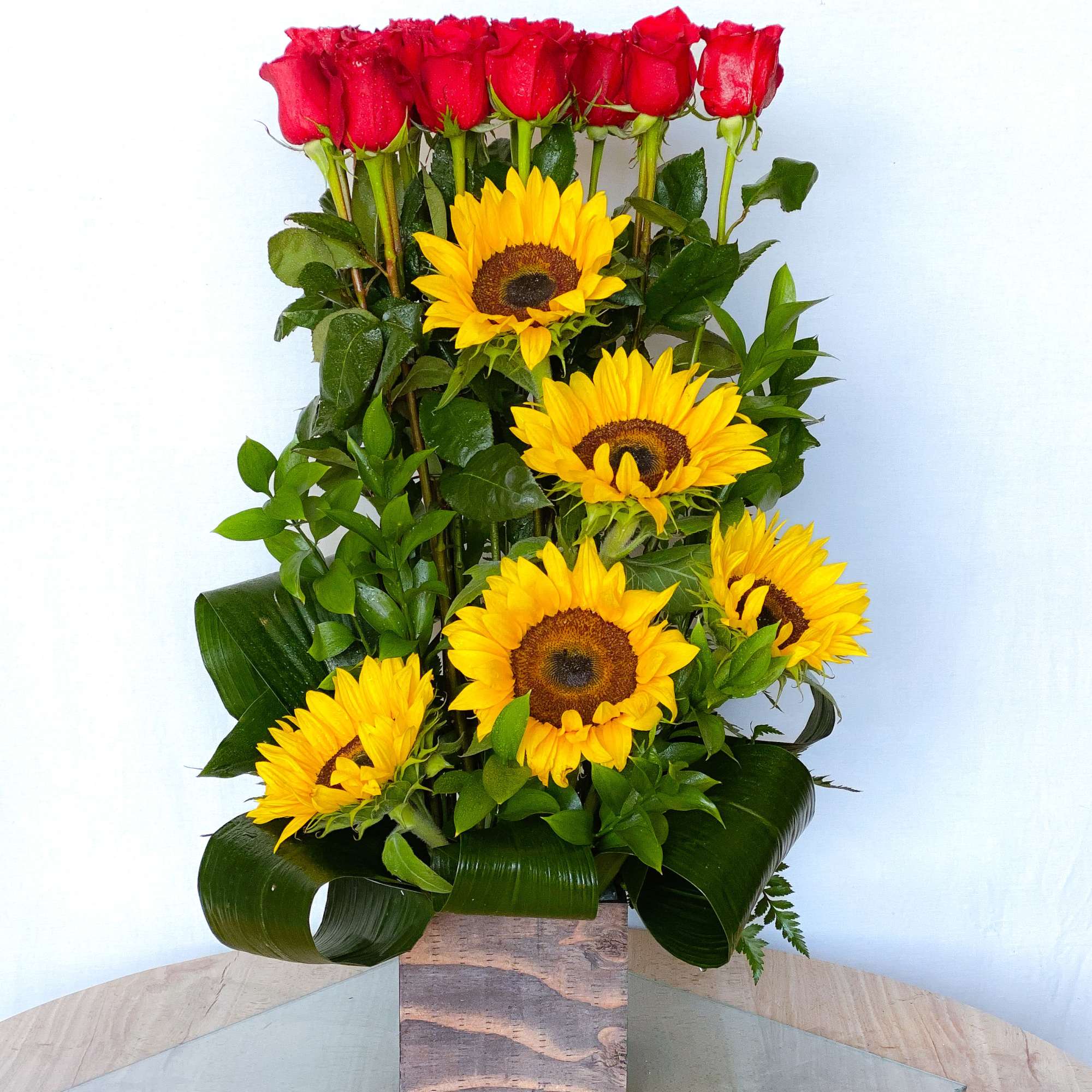 Tall arrangement of red roses and yellow sunflowers in a square vase