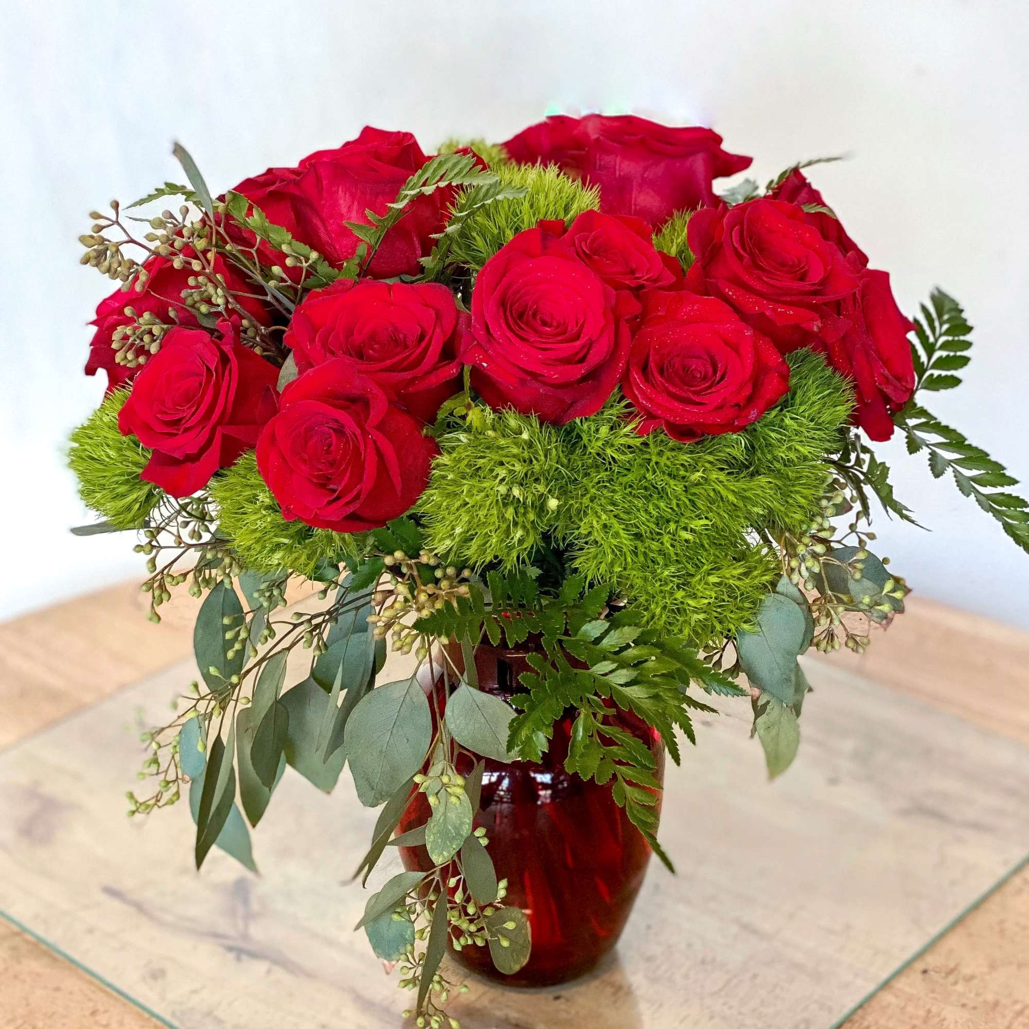 Red roses arranged in a red glass vase with green filler