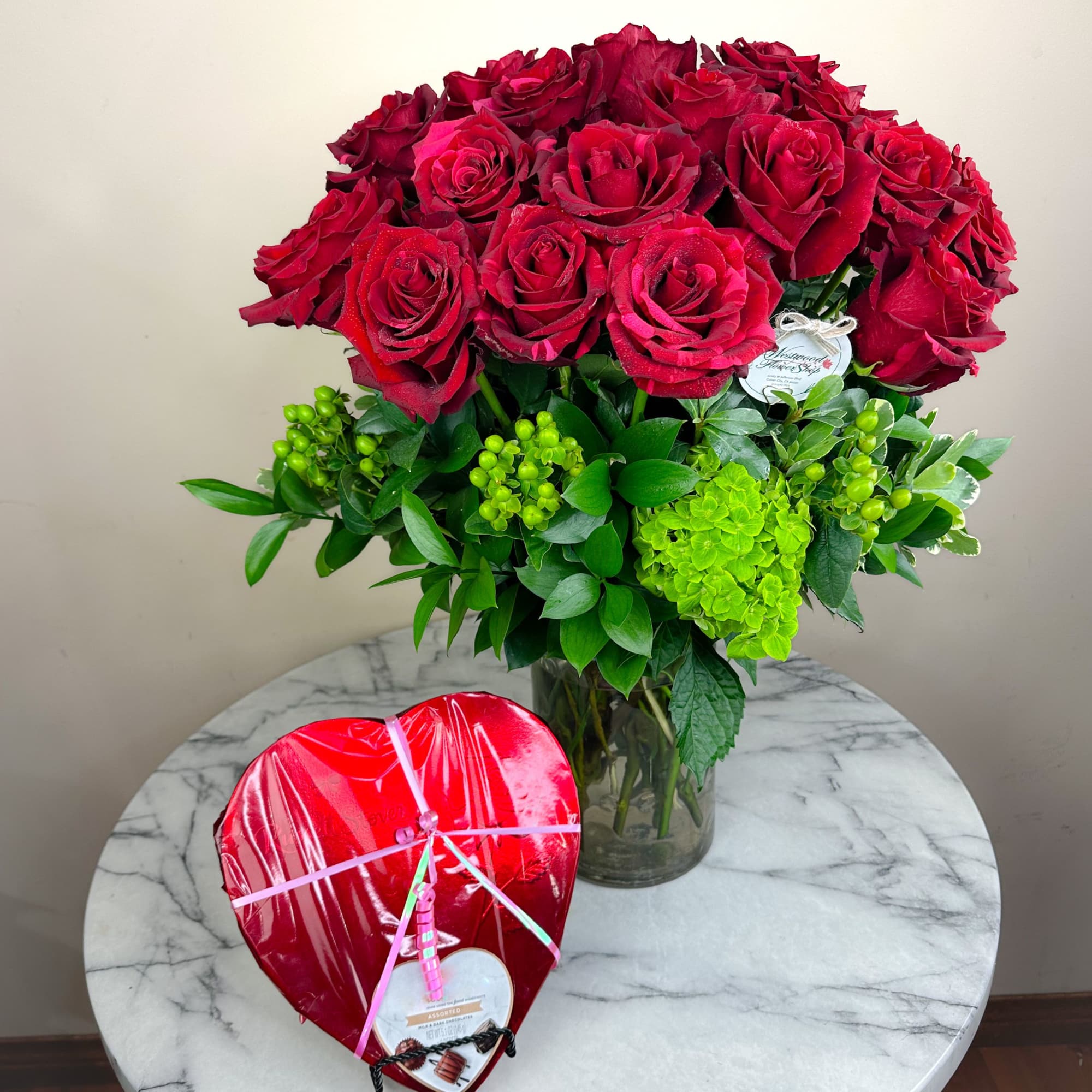 Bouquet of red roses in a glass vase with a heart-shaped box of chocolates