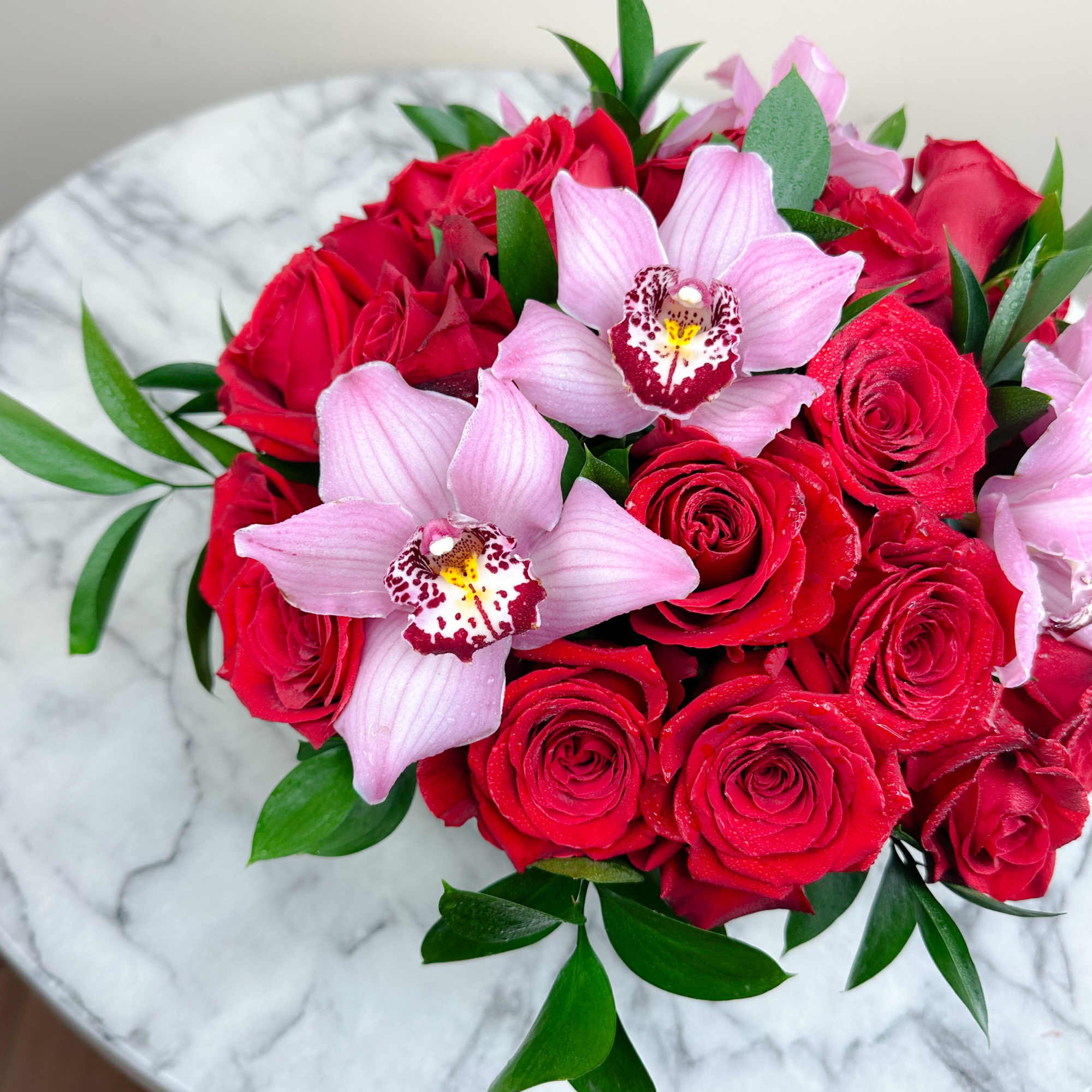 Red roses and pink orchids arranged on a round marble table