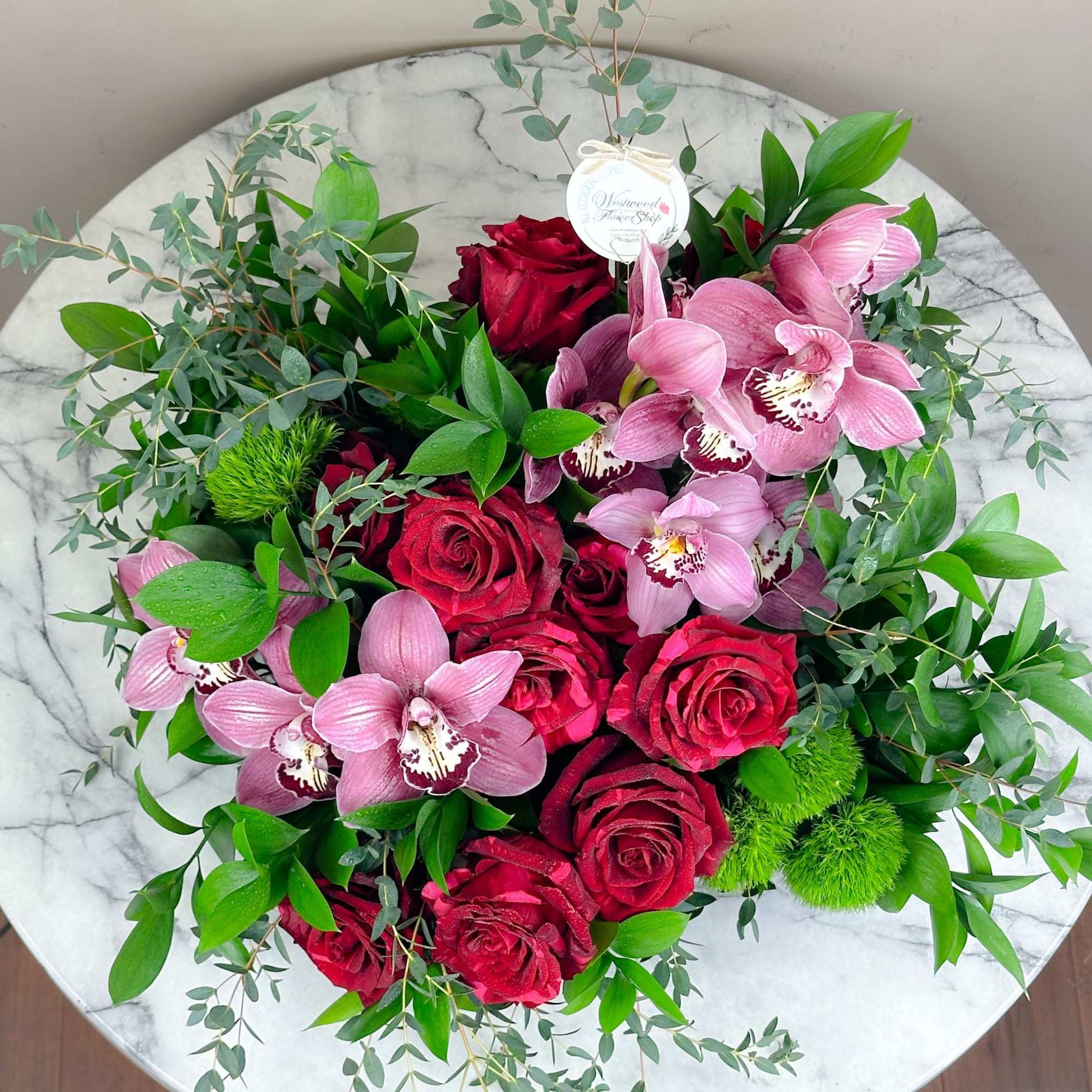 Round bouquet of red roses and pink orchids with green foliage