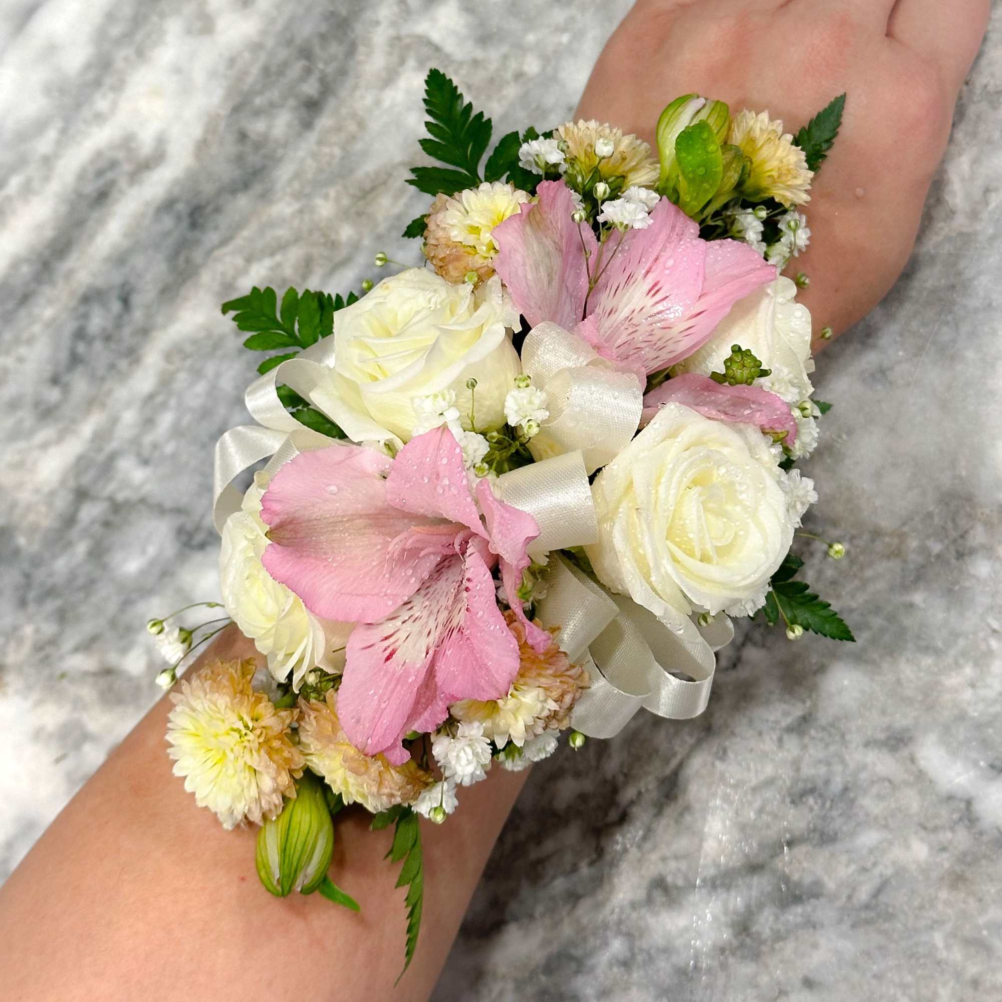 Pink and white floral wrist corsage with ribbon on a person's arm