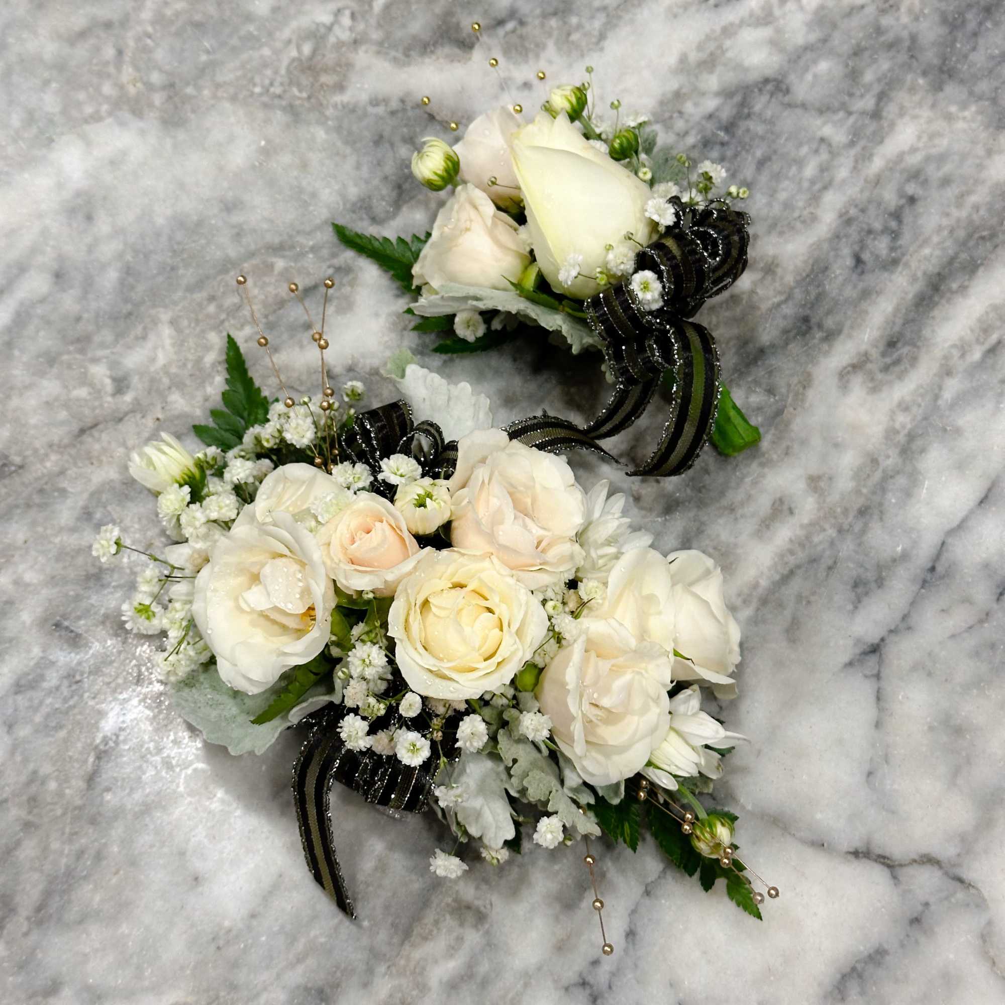 Two white floral corsages with black ribbon accents on a marble surface