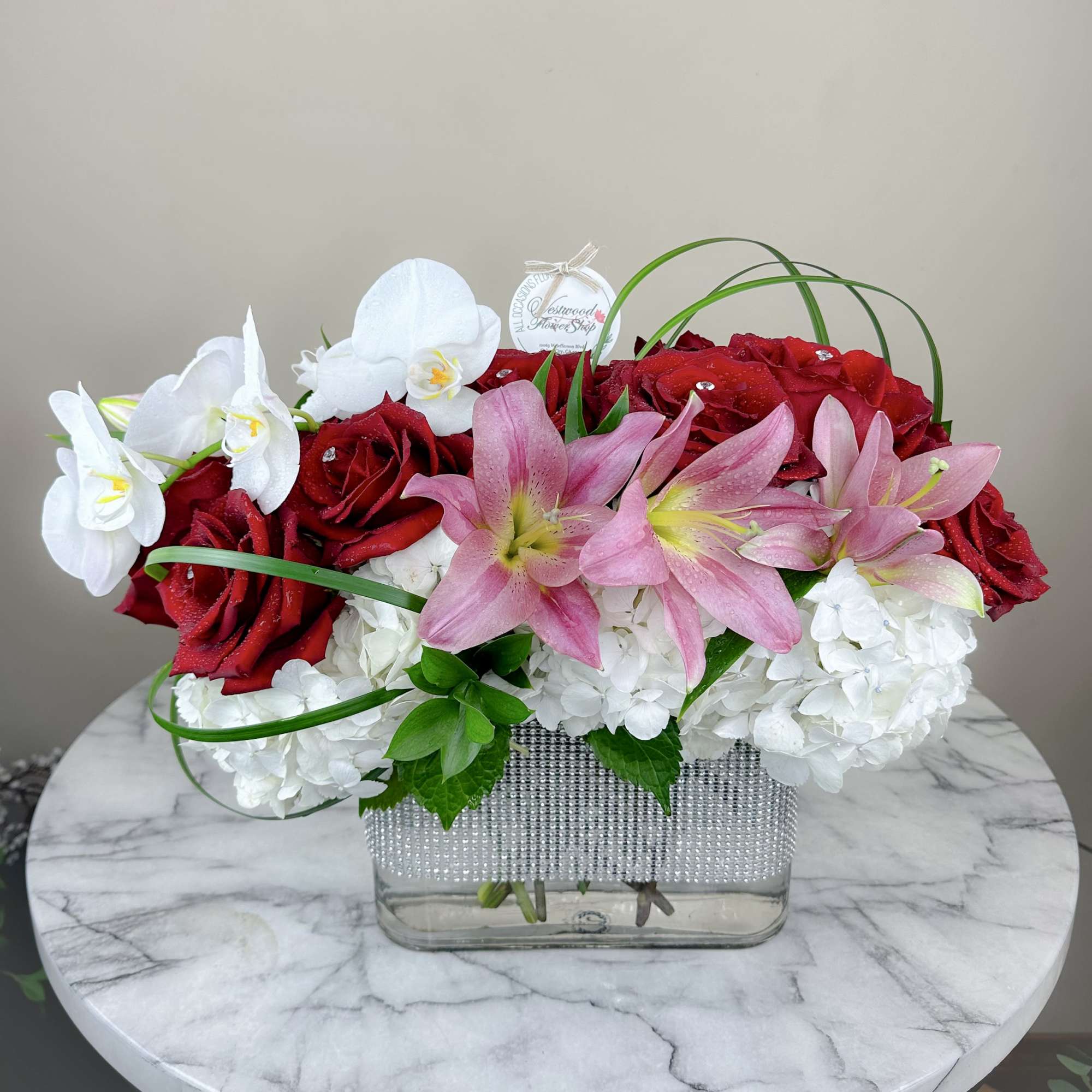 Red roses, pink lilies, and white orchids in a clear rectangular vase