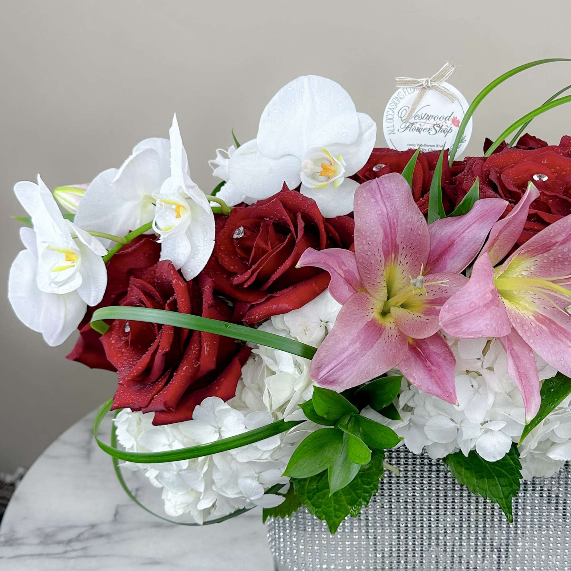 Red roses, white orchids, and pink lilies in a clear vase