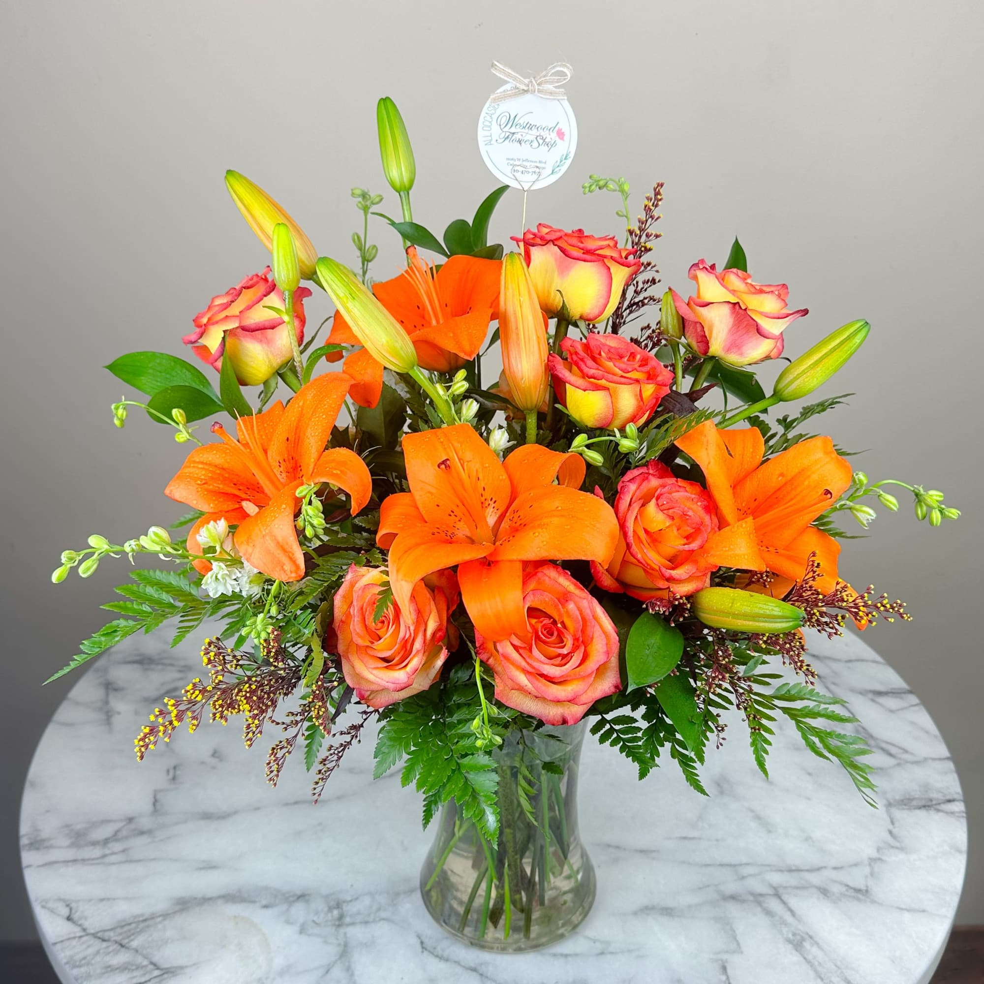 Orange lilies and pink-edged roses arranged in a clear glass vase.