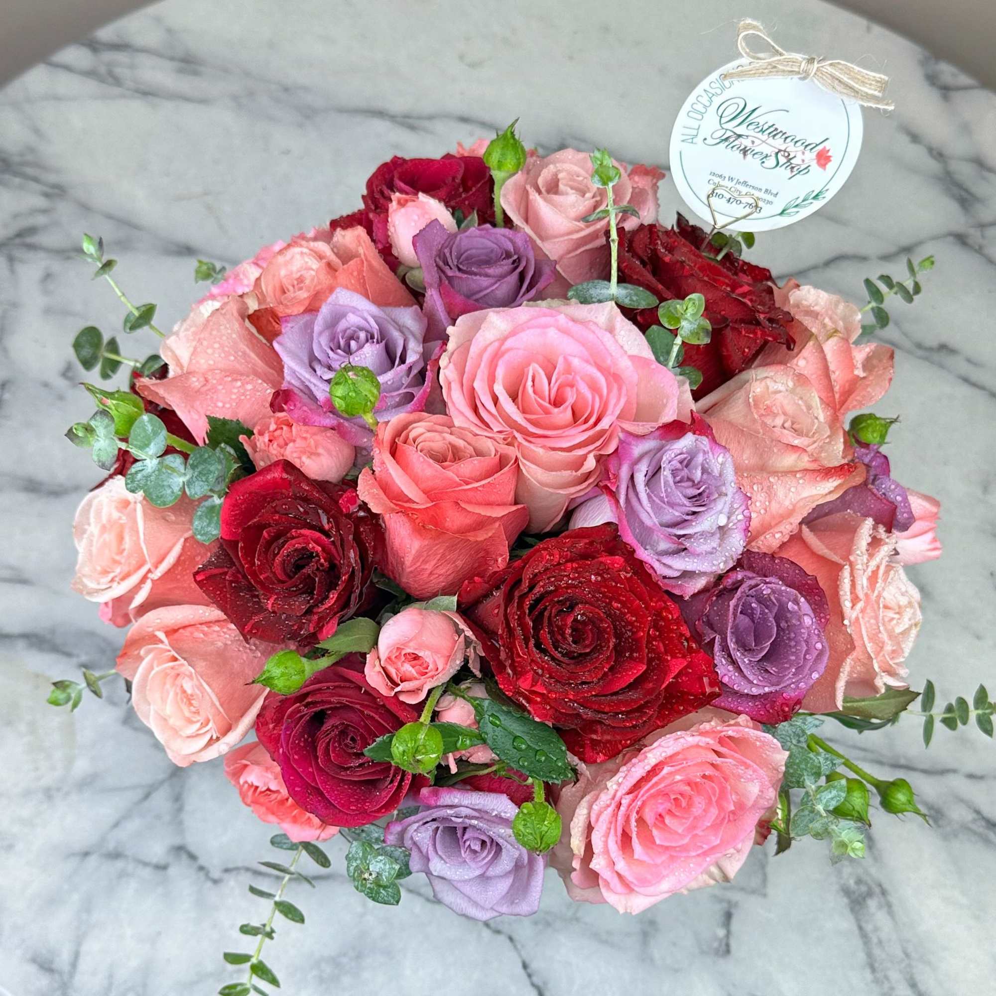 Round bouquet of pink, red, and lavender roses with eucalyptus accents