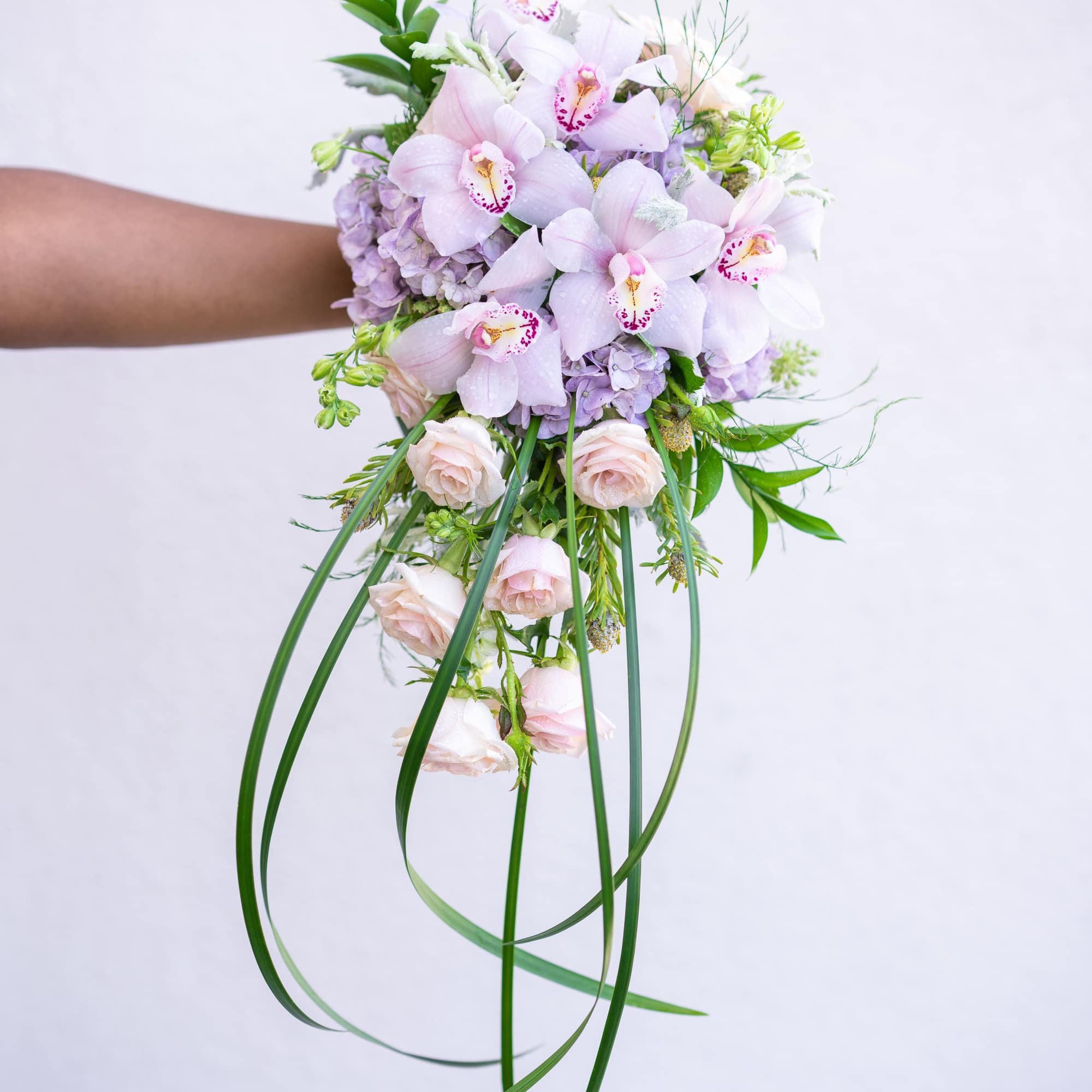 Handheld bouquet of pale pink orchids and roses with long trailing greenery