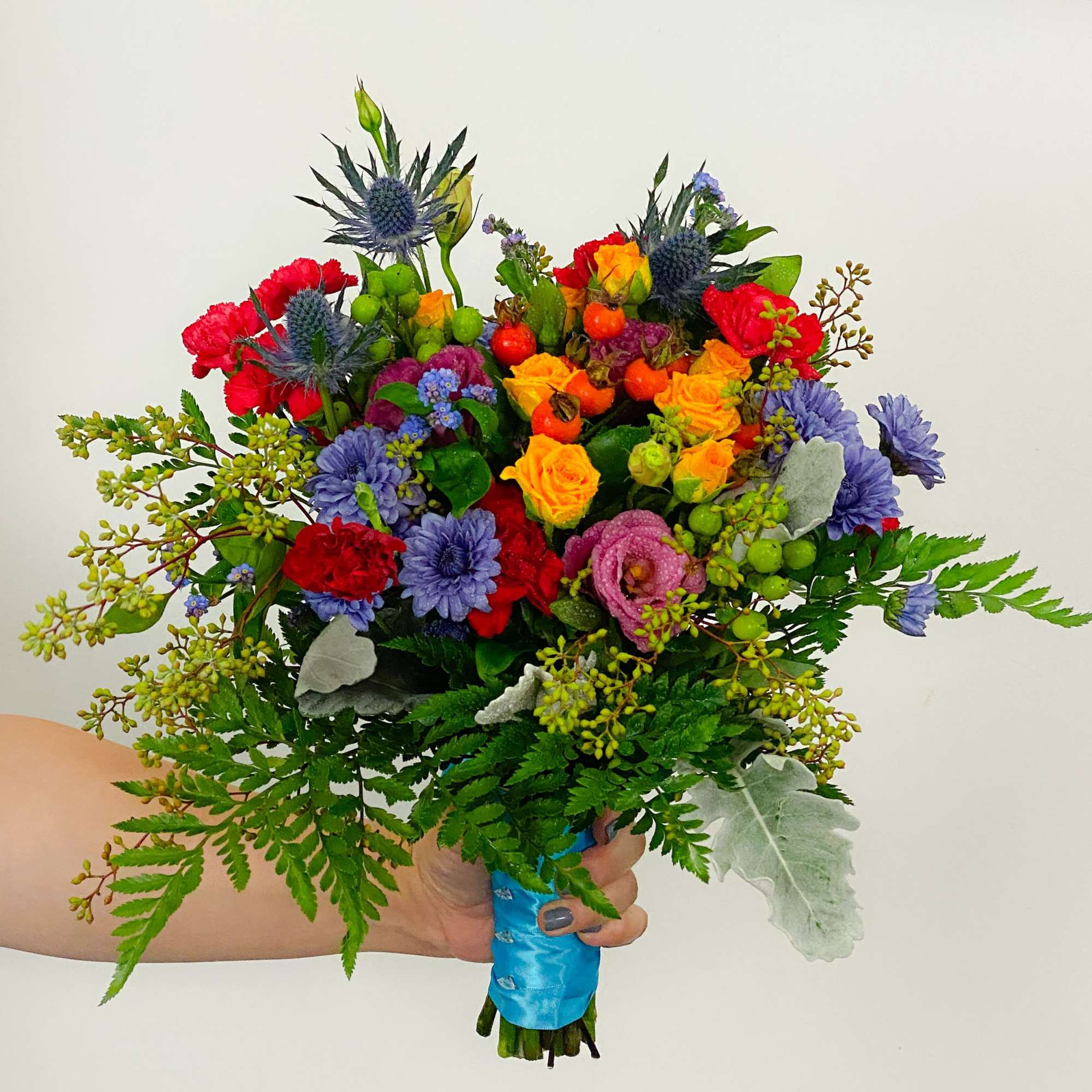 Handheld bouquet of multicolored flowers with blue ribbon wrap