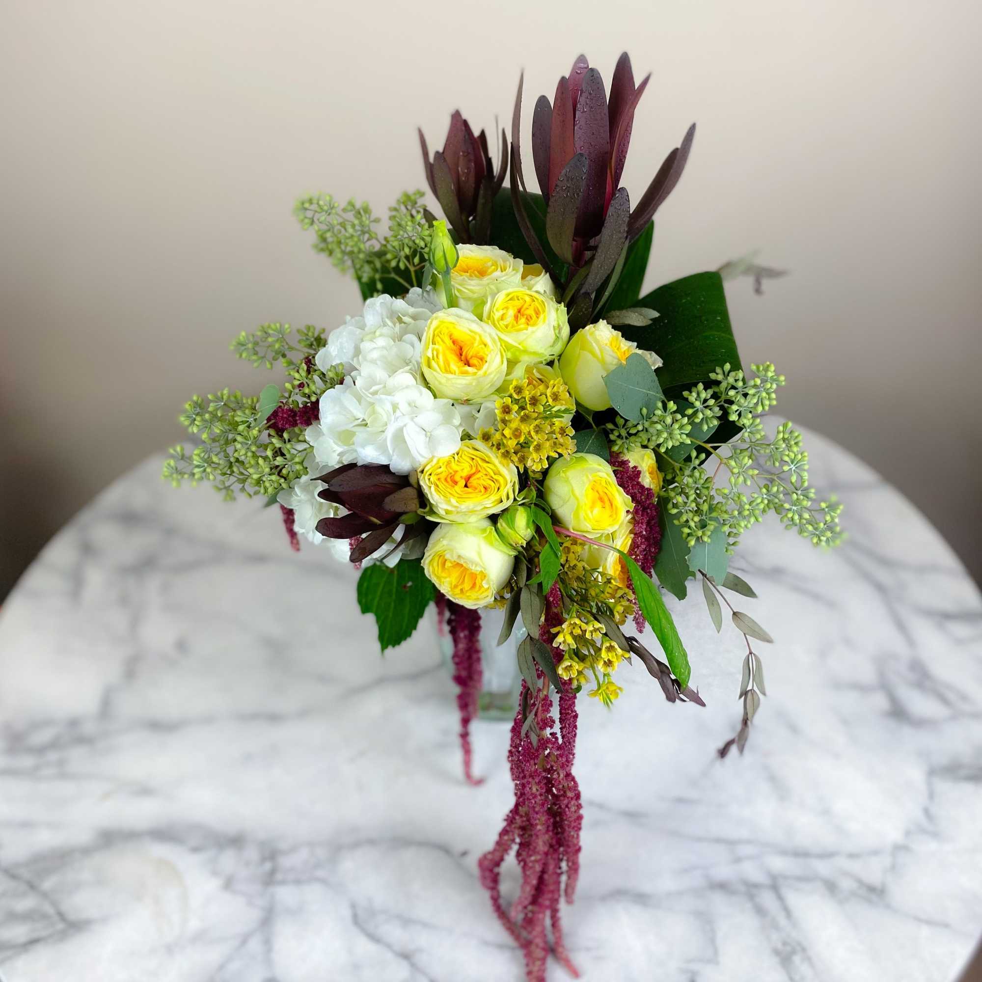 Bouquet of yellow and white flowers with dark foliage in a clear vase
