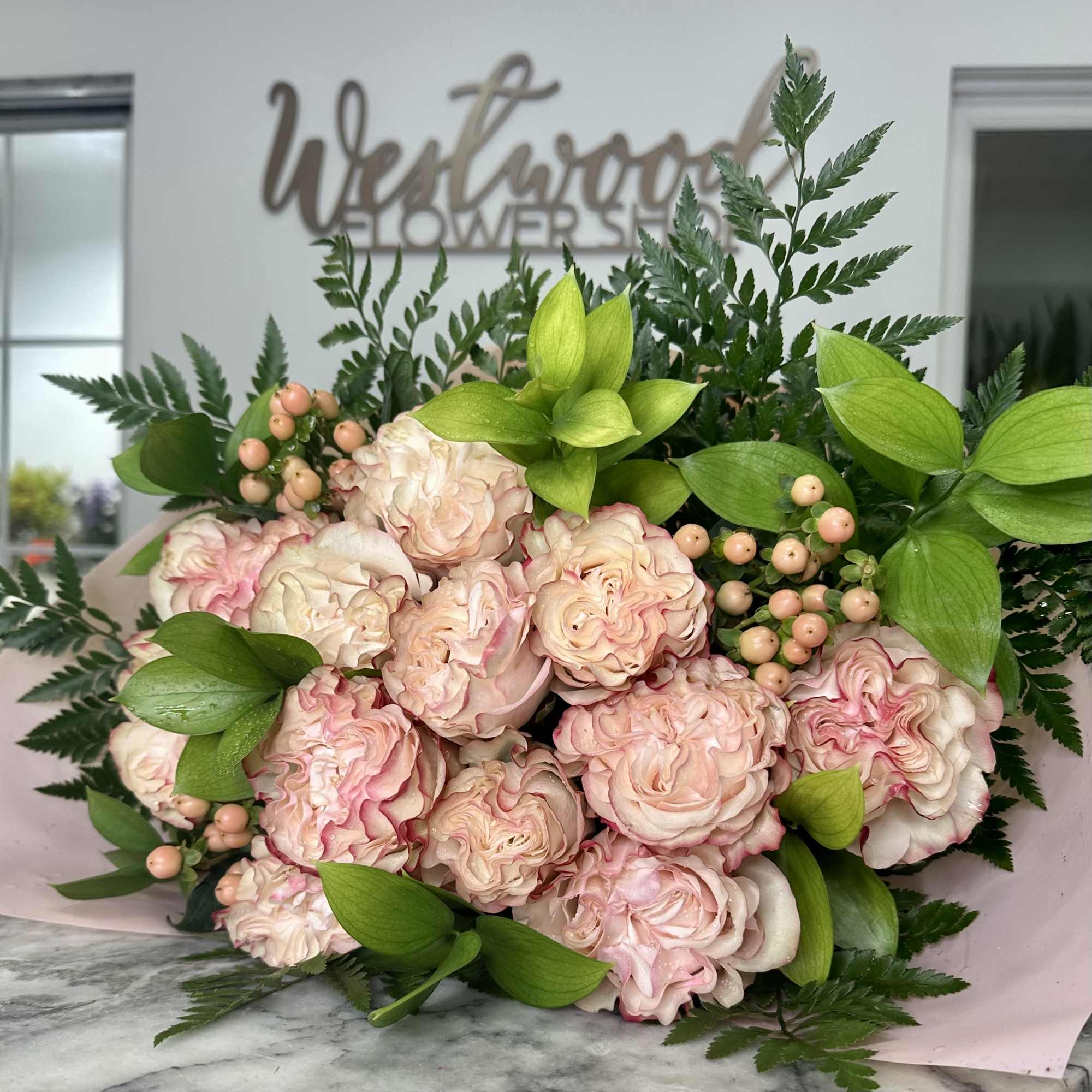 Blush pink roses arranged with bright green foliage and berry accents