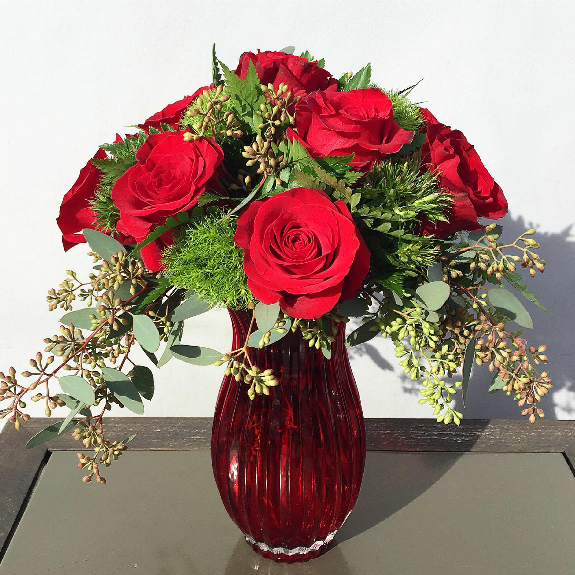 Red roses arranged in a red glass vase with greenery