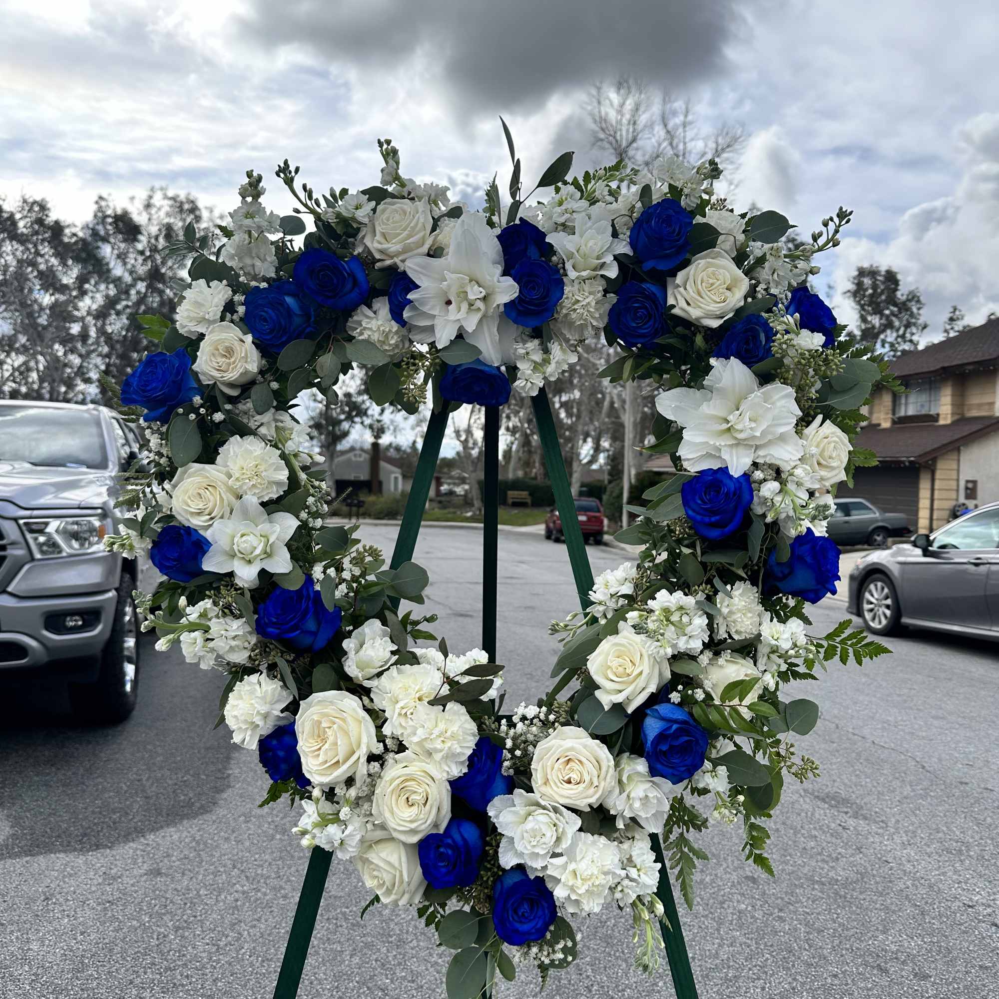 Heart-shaped floral wreath with blue and white roses on a stand